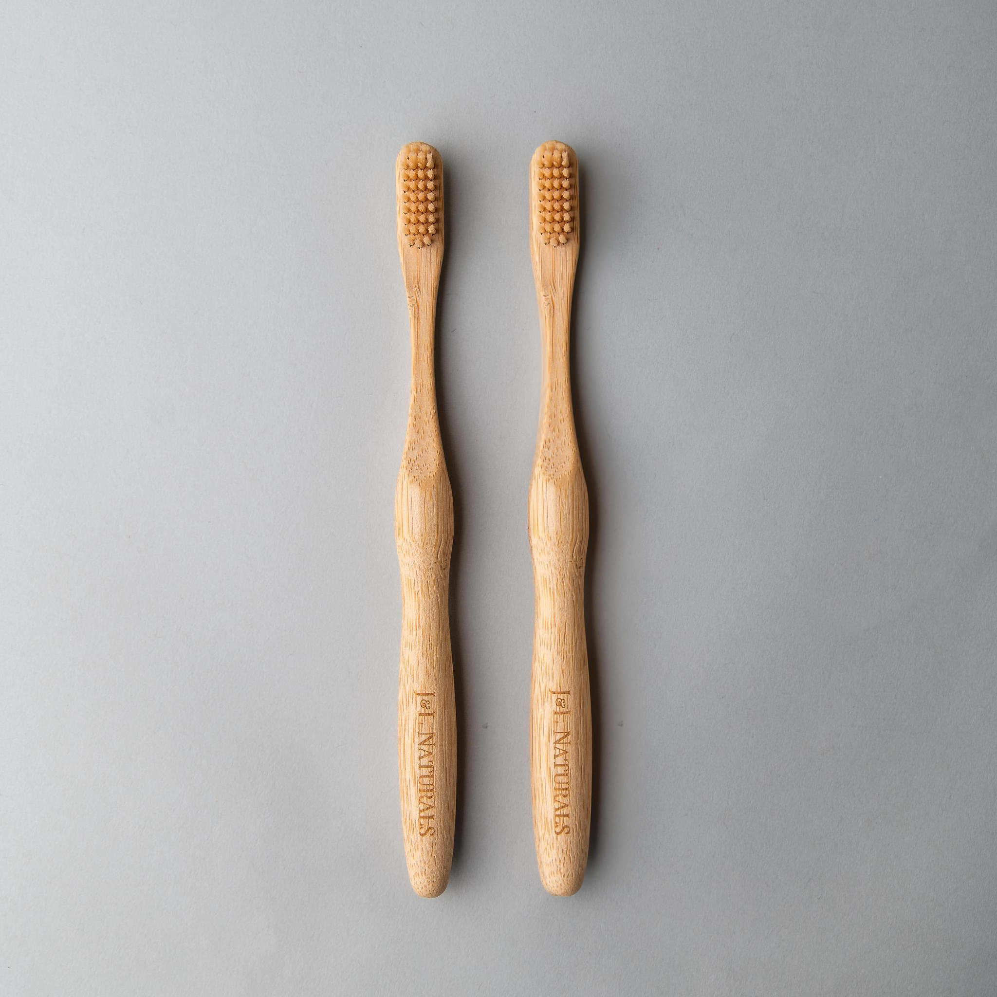 Two bamboo toothbrushes with ergonomic handles and medium wavy bristles, available in various colors.