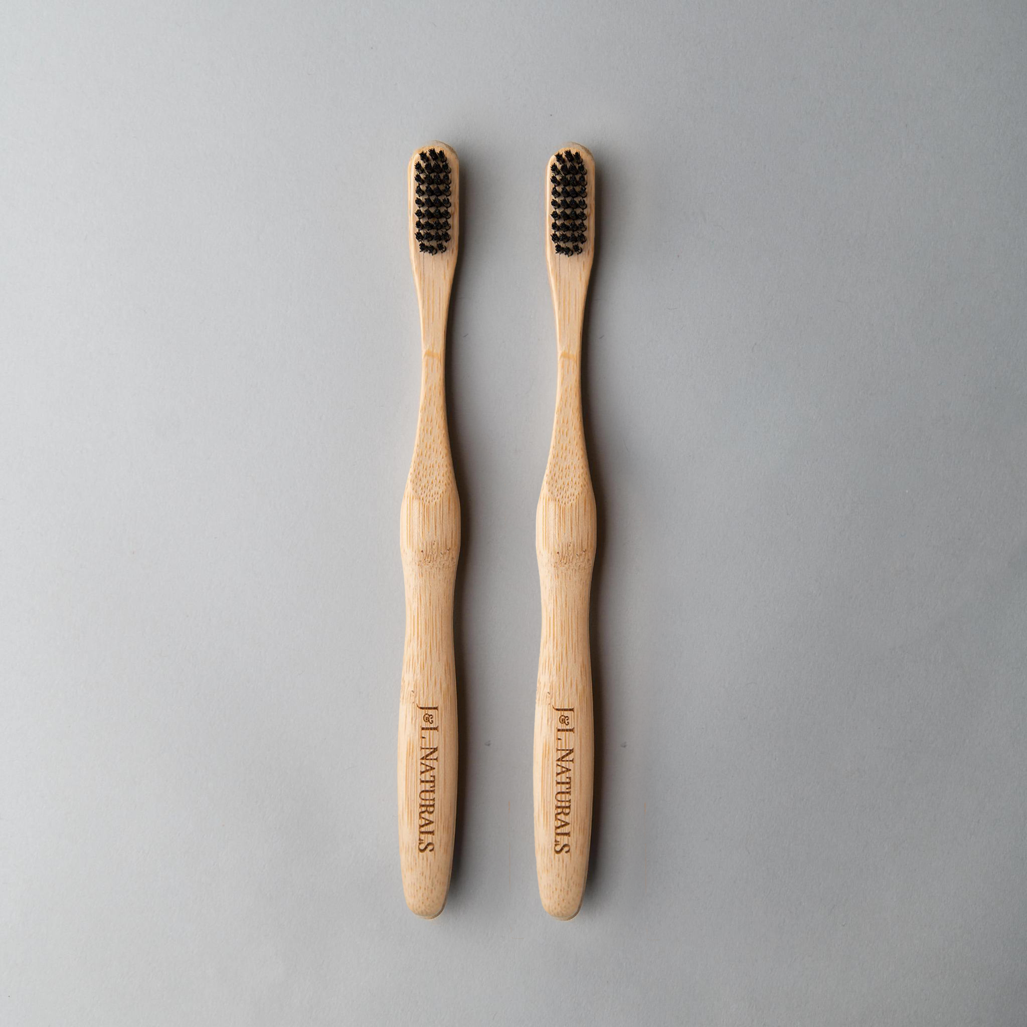 Two bamboo toothbrushes with ergonomic handles and medium wavy bristles, available in various colors.