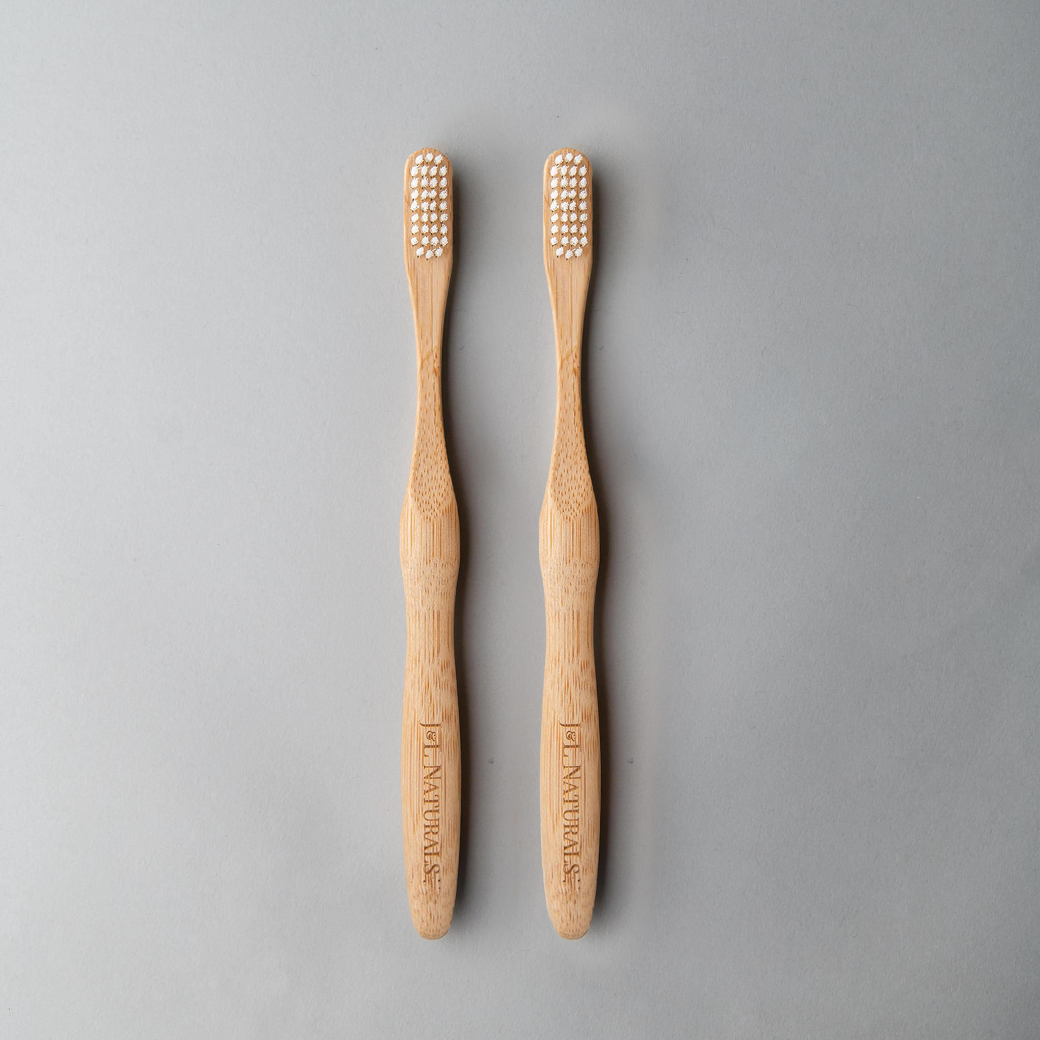 Two bamboo toothbrushes with ergonomic handles and medium wavy bristles, available in various colors.