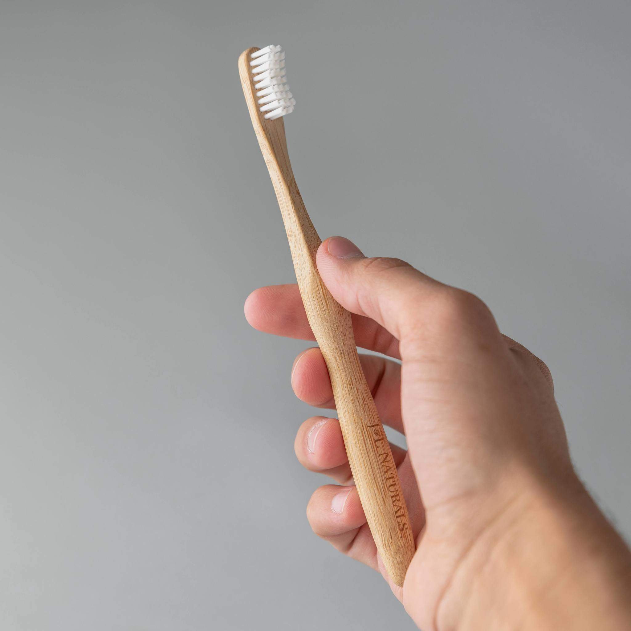 Two bamboo toothbrushes with ergonomic handles and medium wavy bristles, available in various colors.