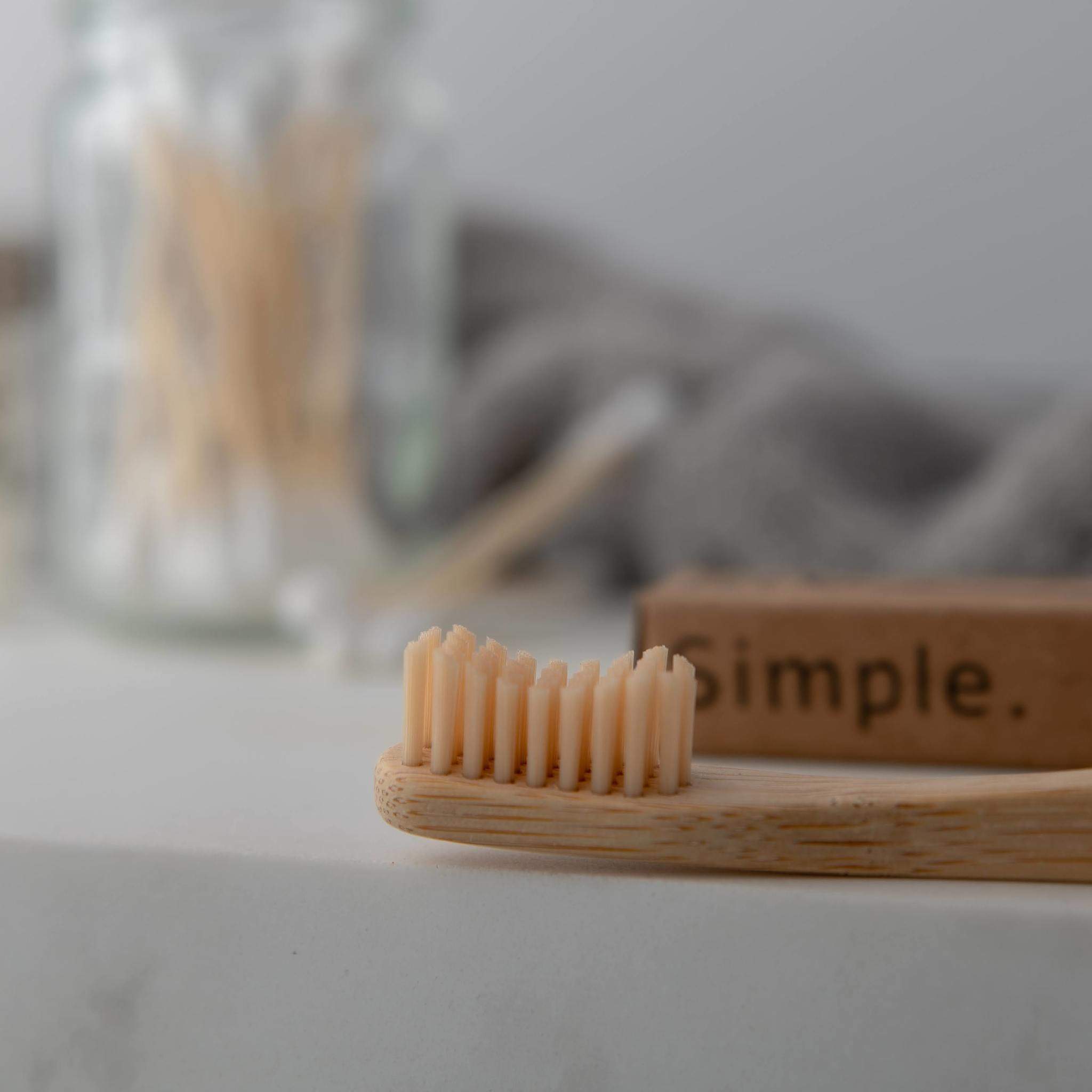 Two bamboo toothbrushes with ergonomic handles and medium wavy bristles, available in various colors.