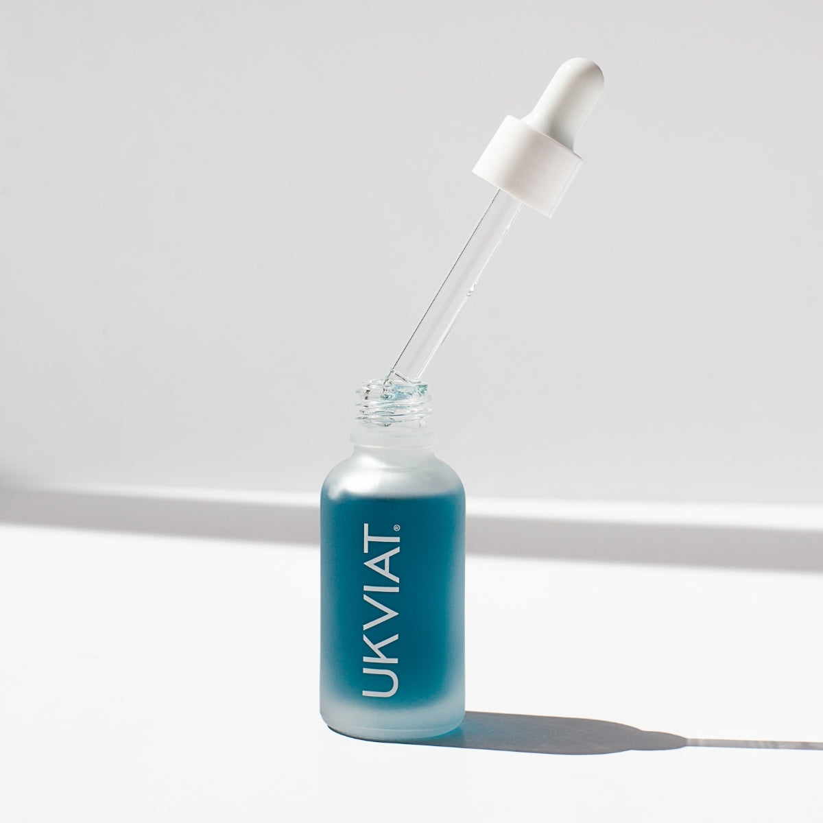 A bottle of blue balancing facial serum with a dropper, showcasing its clear liquid and elegant packaging, set against a soft background.