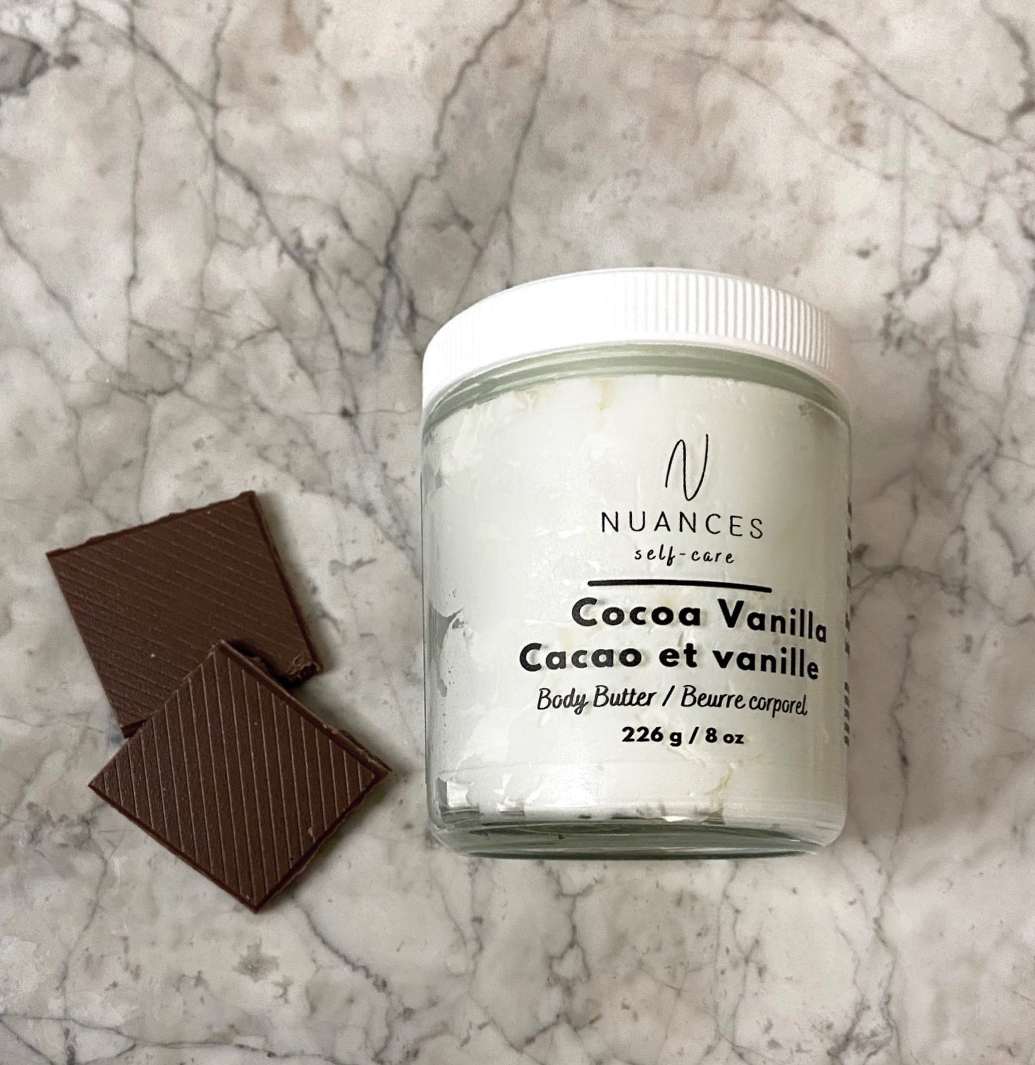 A jar of Cocoa Vanilla Body Butter with a creamy texture, showcasing its rich cocoa color and luxurious packaging.