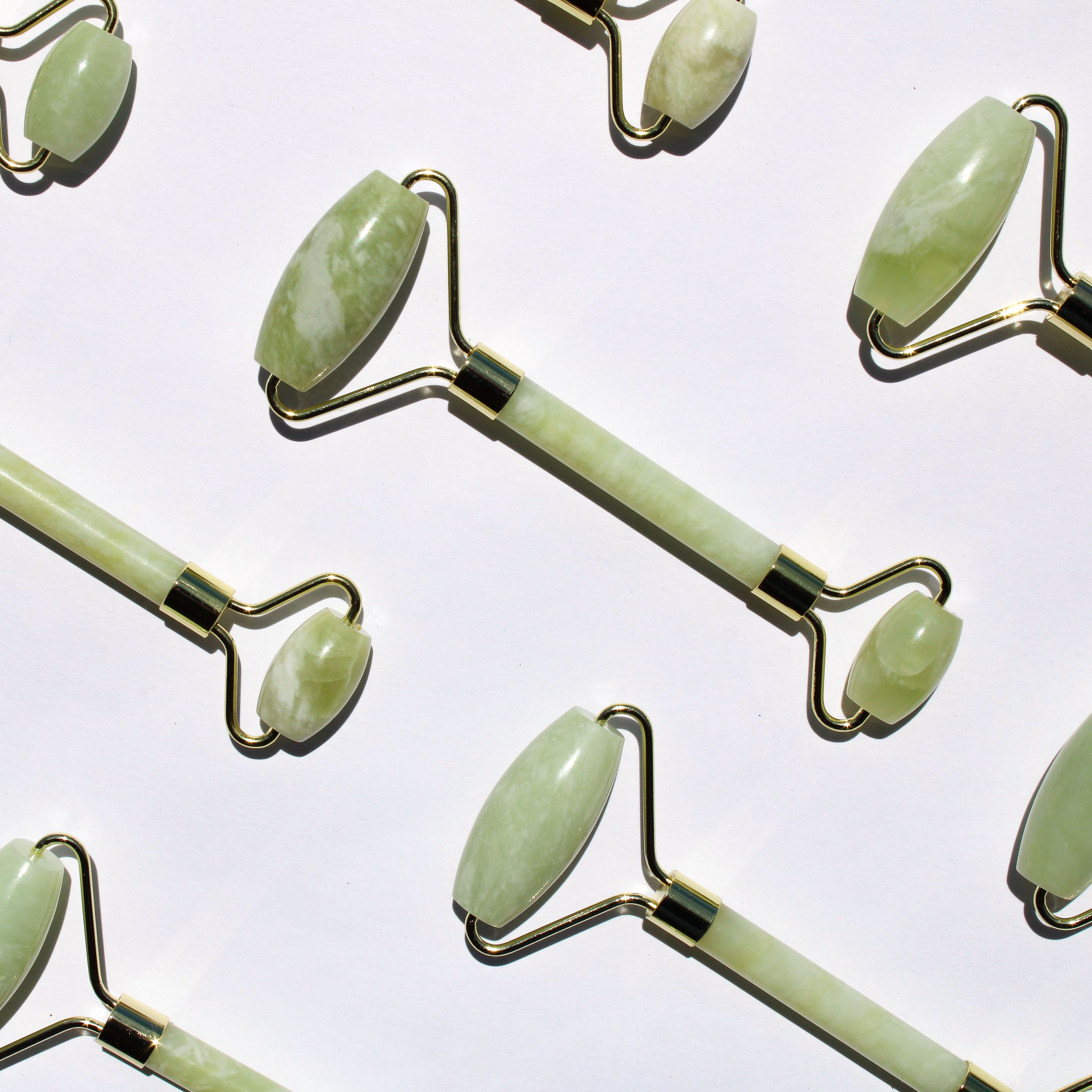 A jade facial roller resting on a marble surface, showcasing its smooth jade stone and dual-ended design for facial massage.