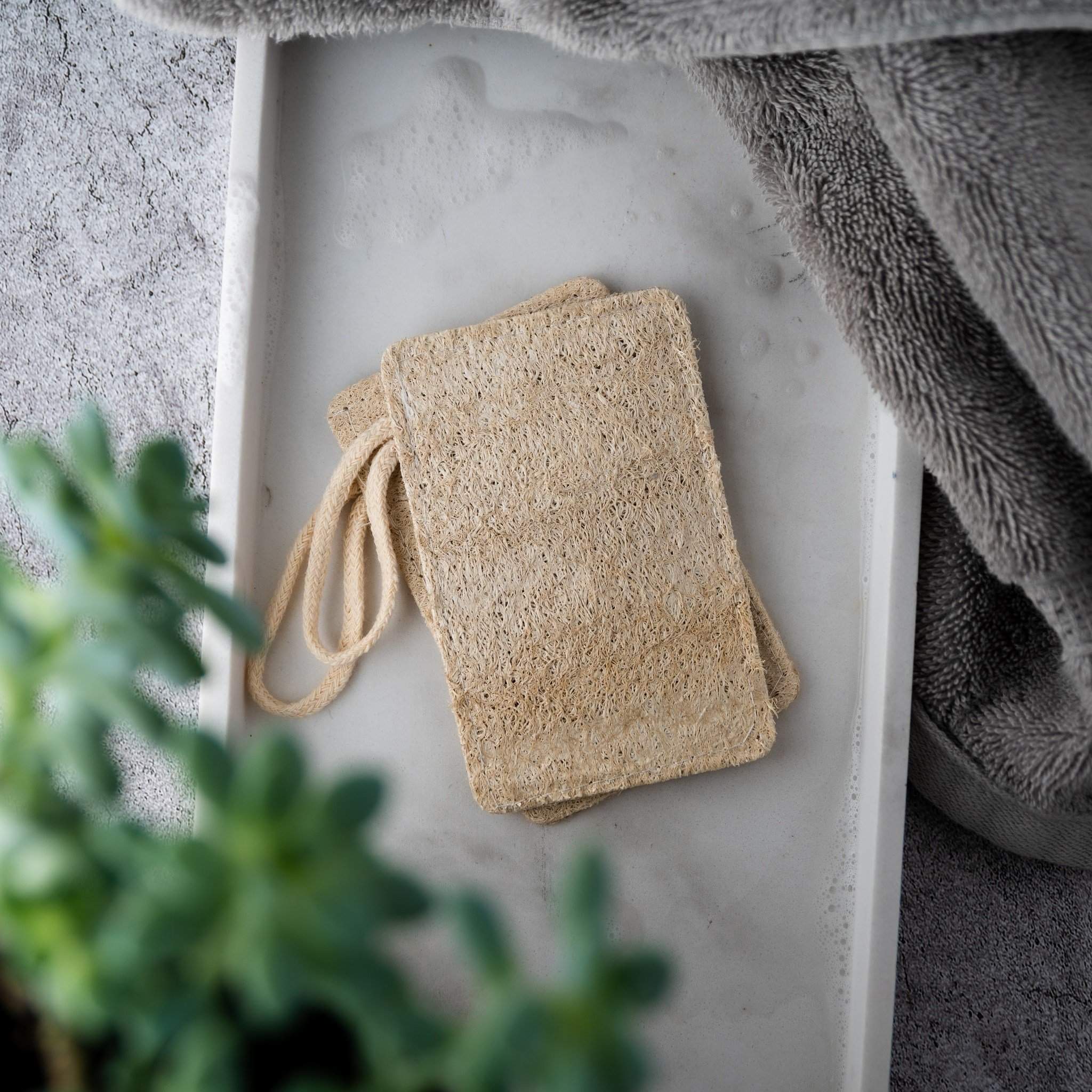 Two natural loofah pads on a wooden surface, showcasing their texture and eco-friendly design.