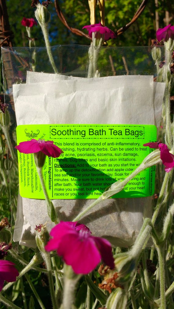 Three organic soothing bathtub tea bags filled with nutrient-rich herbs for skin care, displayed on a wooden surface.