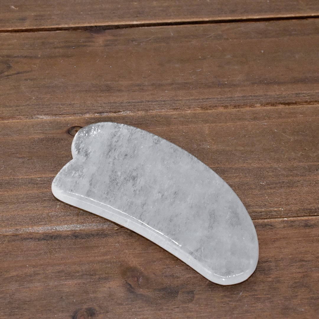 A clear quartz Gua Sha massage tool designed for facial and body massage, showcasing its smooth edges and natural stone texture.