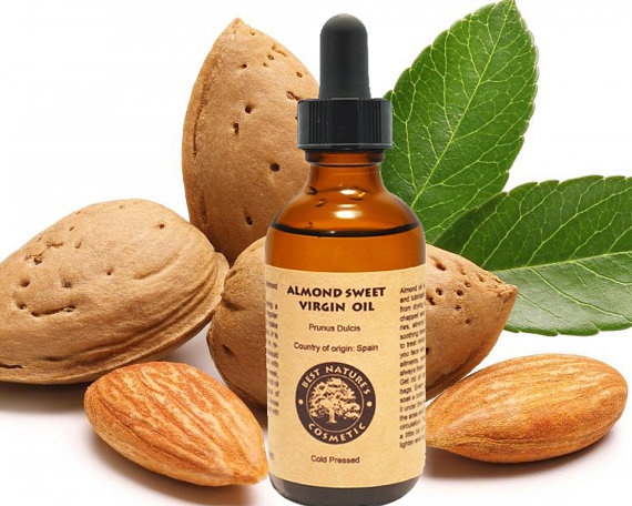 A bottle of organic almond oil with a pale yellow liquid, surrounded by almonds and a cotton ball, showcasing its moisturizing properties for reducing dark circles.