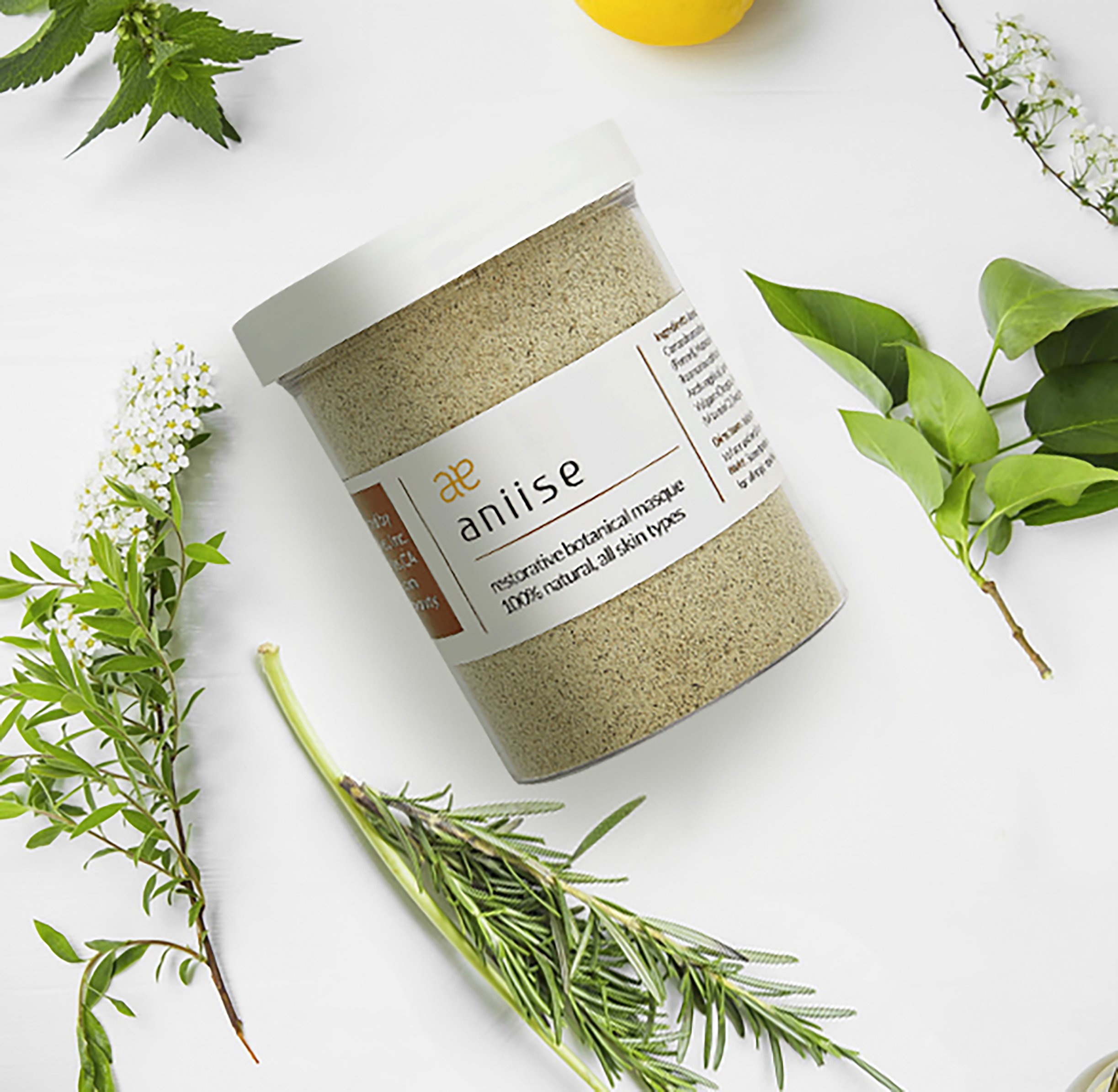 Restorative Botanical Face Mask in a jar with natural herbs and flowers surrounding it, showcasing its organic ingredients.