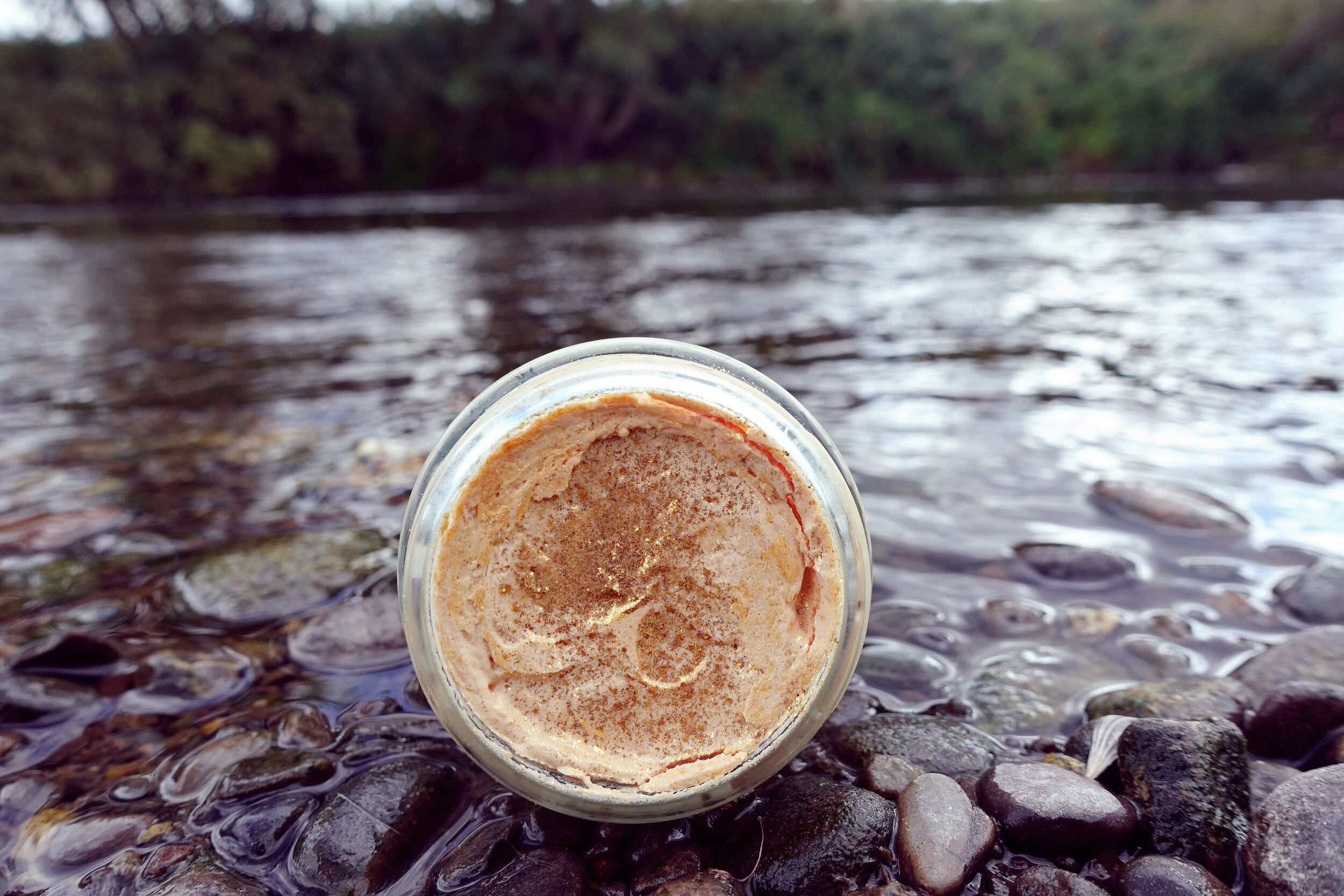 A jar of Shim Shimmer Body Butter showcasing its creamy texture and golden shimmer, surrounded by natural ingredients like shea butter and essential oils.