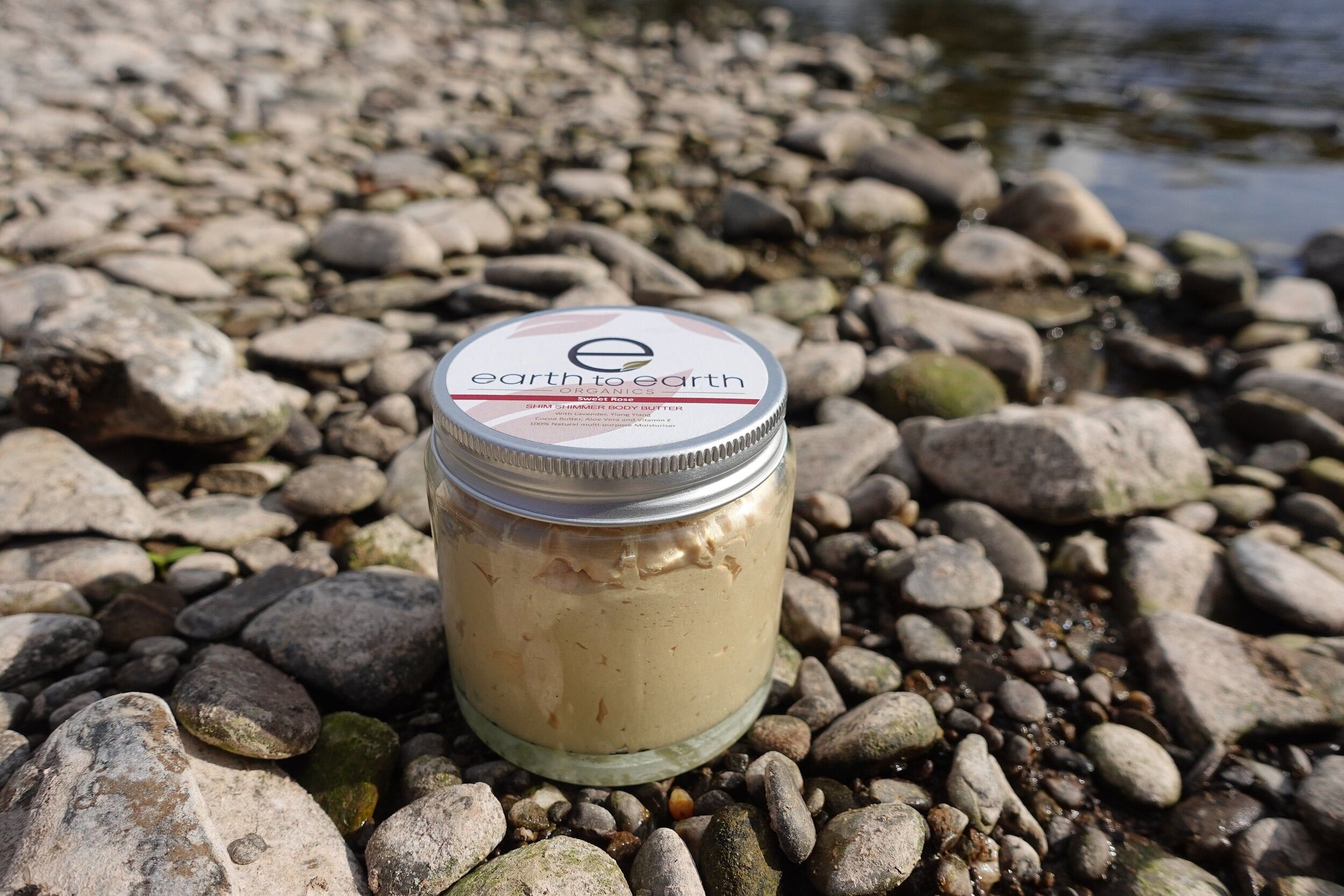 A jar of Shim Shimmer Body Butter showcasing its creamy texture and golden shimmer, surrounded by natural ingredients like shea butter and essential oils.