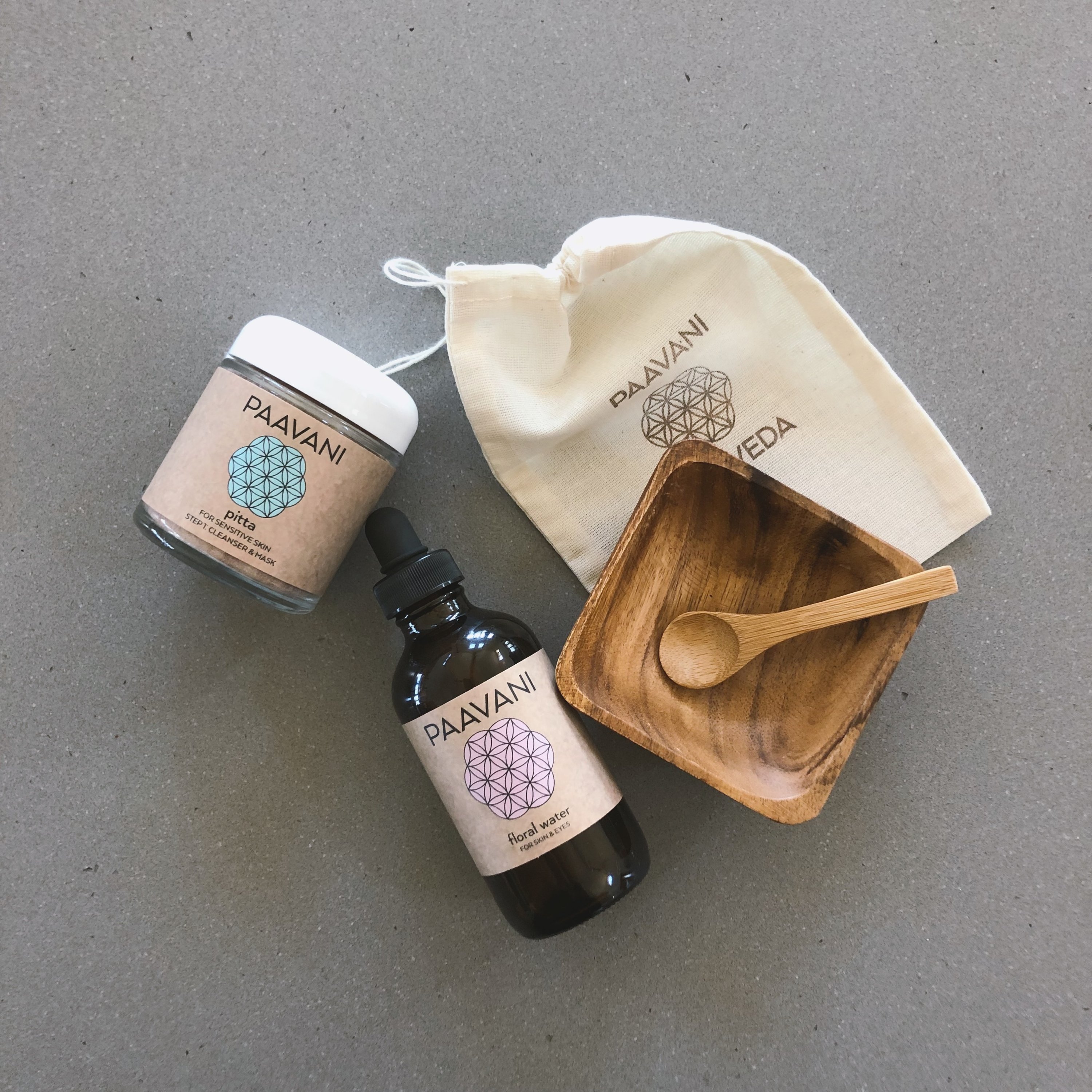 The Cleanser & Mask Ritual set including powdered herbs, floral water, acacia bowl, bamboo spoon, and muslin pouch for skincare.