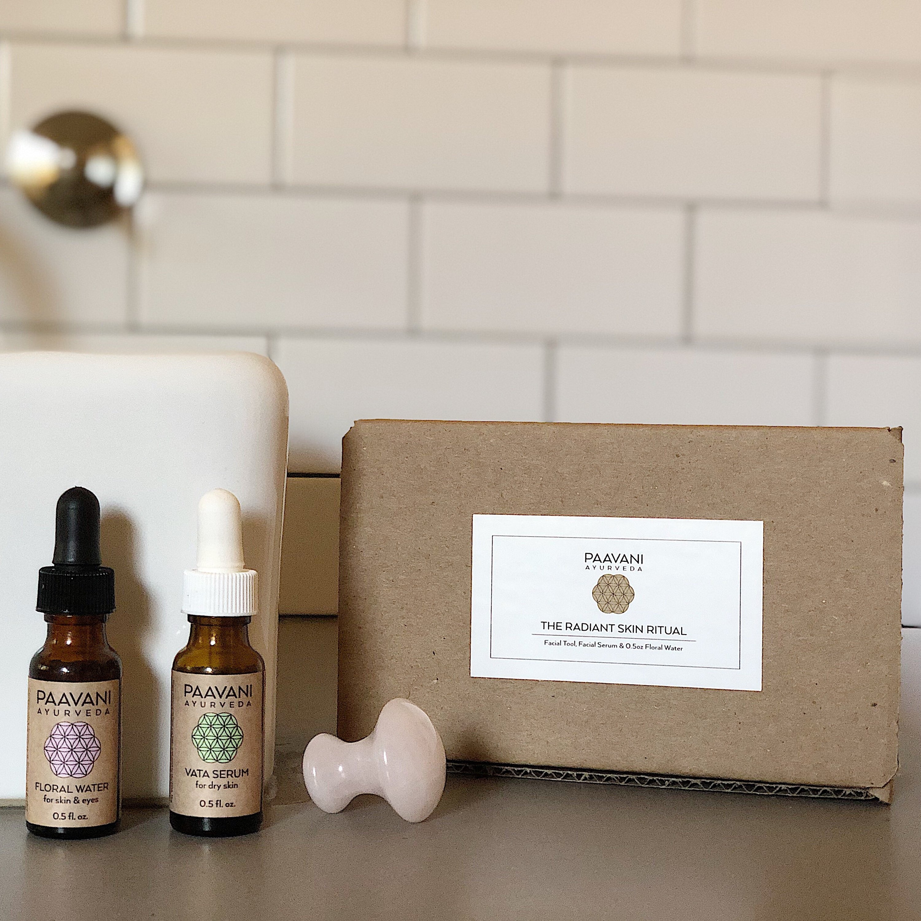 The Radiant Skin Ritual kit featuring the Kansa Wand Facial Tool, facial serum, floral water, and a travel pouch, all designed for at-home facial massages.