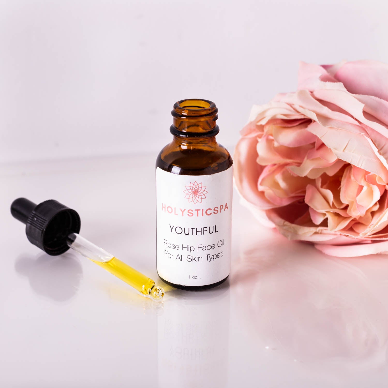 A bottle of Youthful Rosehip Face Oil with a dropper, surrounded by natural ingredients like rose hips and essential oils, showcasing its organic formulation.