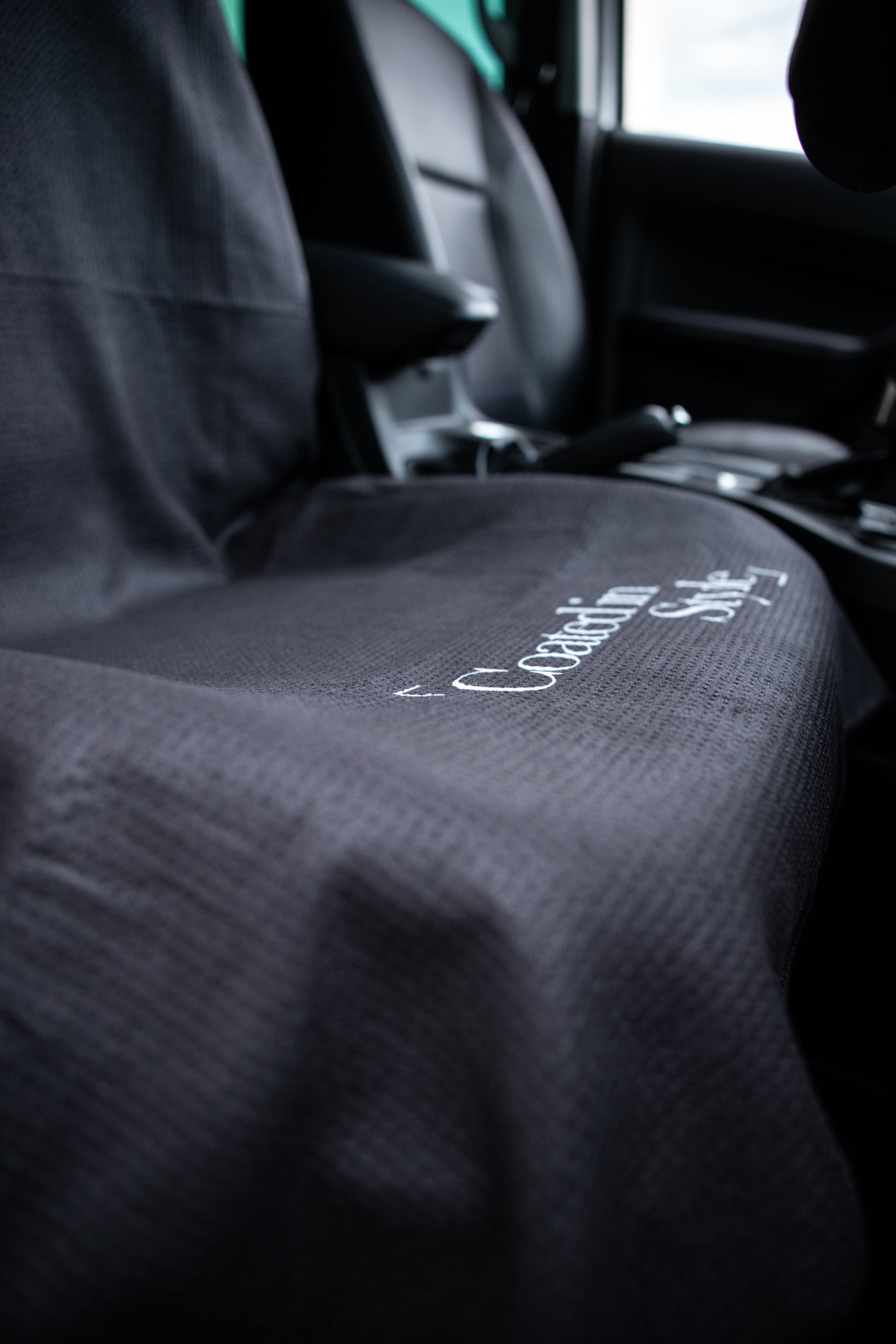 THE OG TOWEL in sleek black color, designed for car seats and beach use, showcasing its hooded shape and microfiber material.