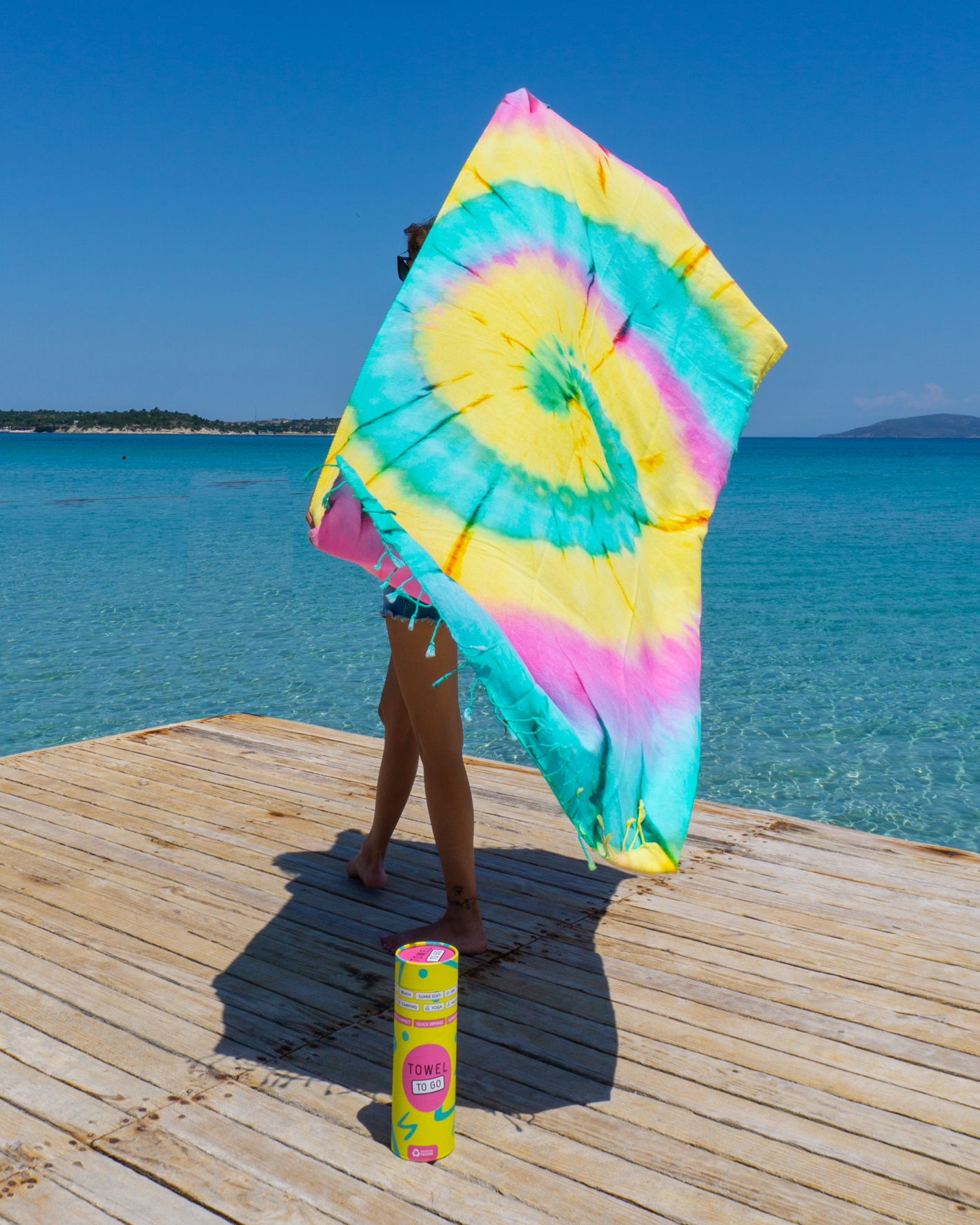 A vibrant pink and green tie-dye convertible towel kimono displayed on a sandy beach, showcasing its stylish design and eco-friendly fabric.