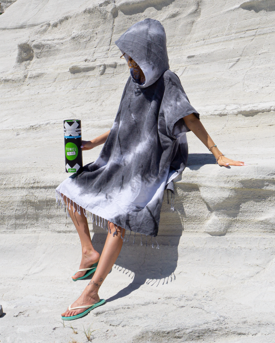 A stylish black and white tie dye hooded beach poncho displayed on a sandy beach, showcasing its unique patterns and relaxed fit.