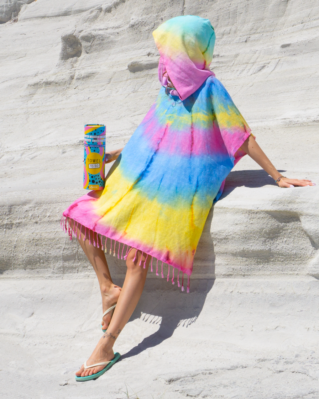 A vibrant blue and yellow tie dye hooded beach poncho displayed on a sandy beach, showcasing its unique patterns and relaxed fit.