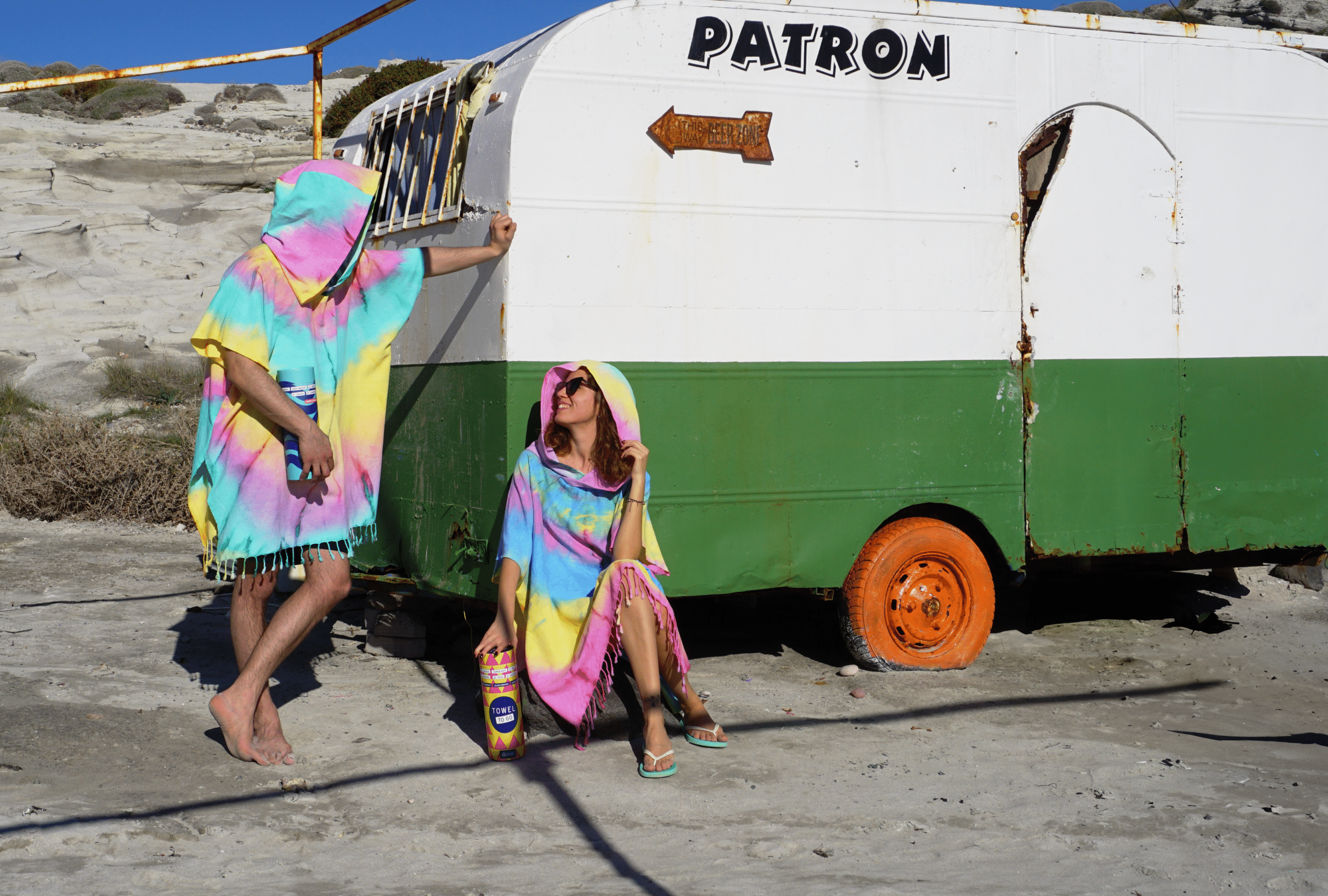 A vibrant blue and yellow tie dye hooded beach poncho displayed on a sandy beach, showcasing its unique patterns and relaxed fit.