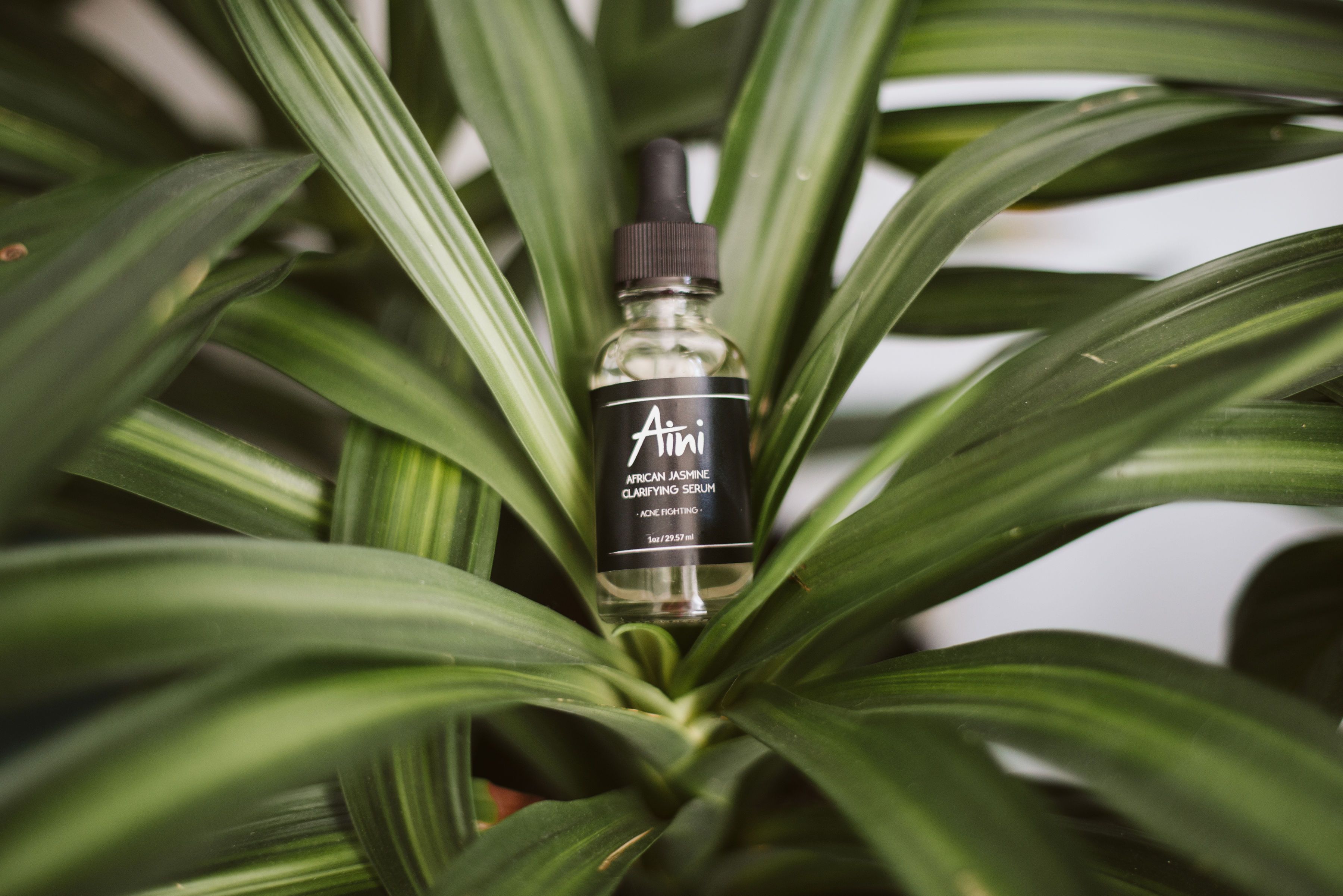 A bottle of African Jasmine Clarifying Serum with a dropper, showcasing its clear liquid and elegant packaging, surrounded by jasmine flowers.