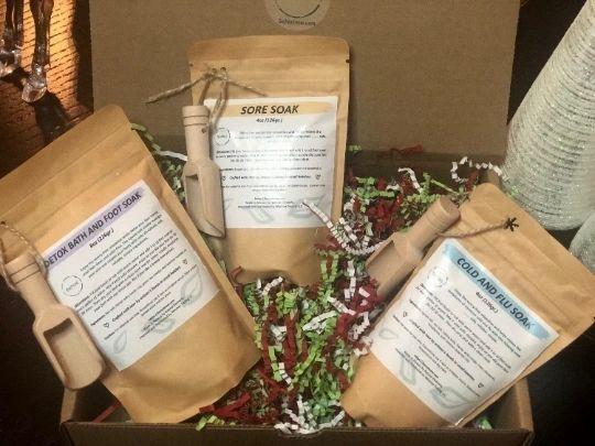 A beautifully packaged Bath and Foot Soak in a kraft bag with a mini bamboo scoop, showcasing natural ingredients like sea salts and lavender.