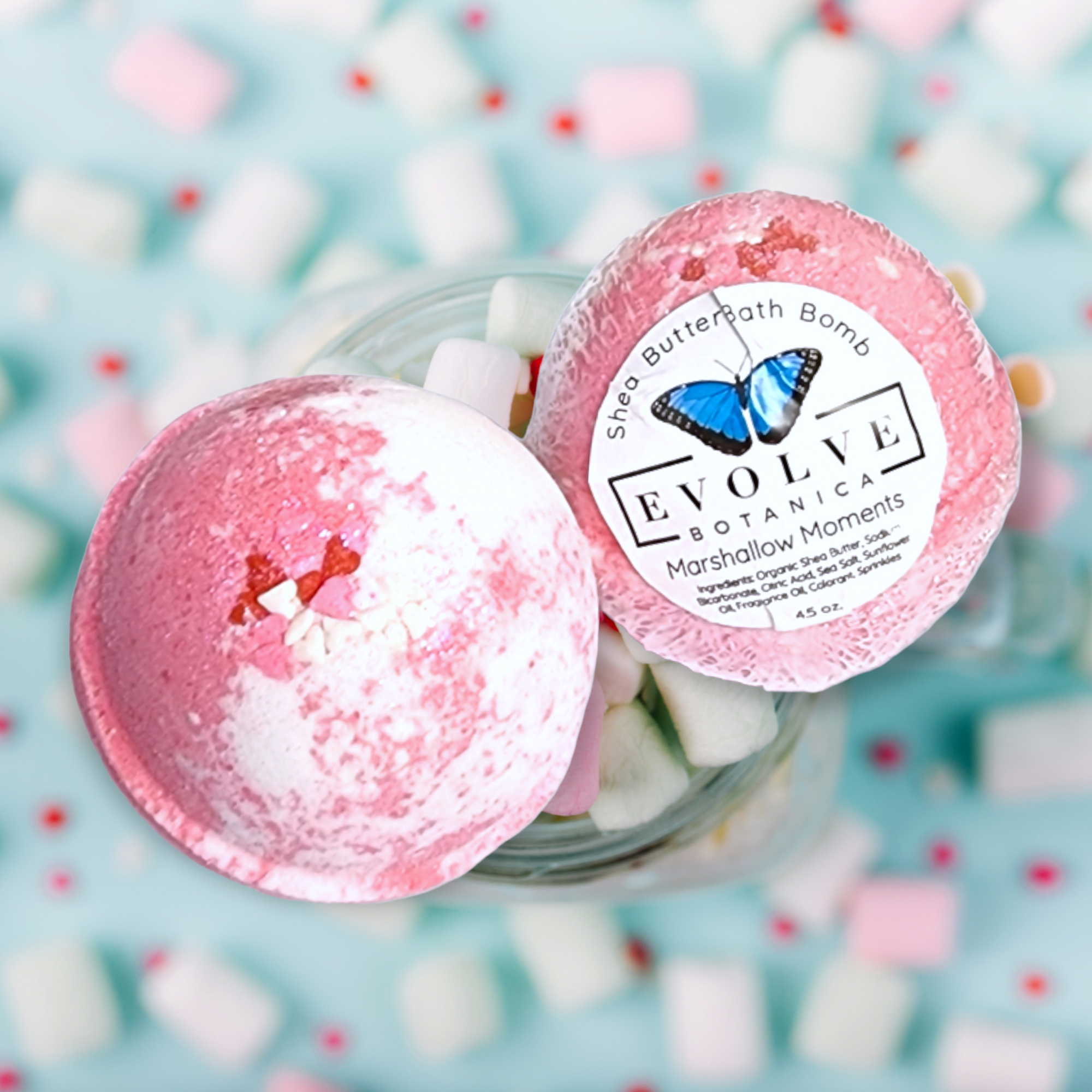 A colorful Marshmallow Moments Bath Bomb with swirls of pink and white, surrounded by marshmallows and sugared plums.