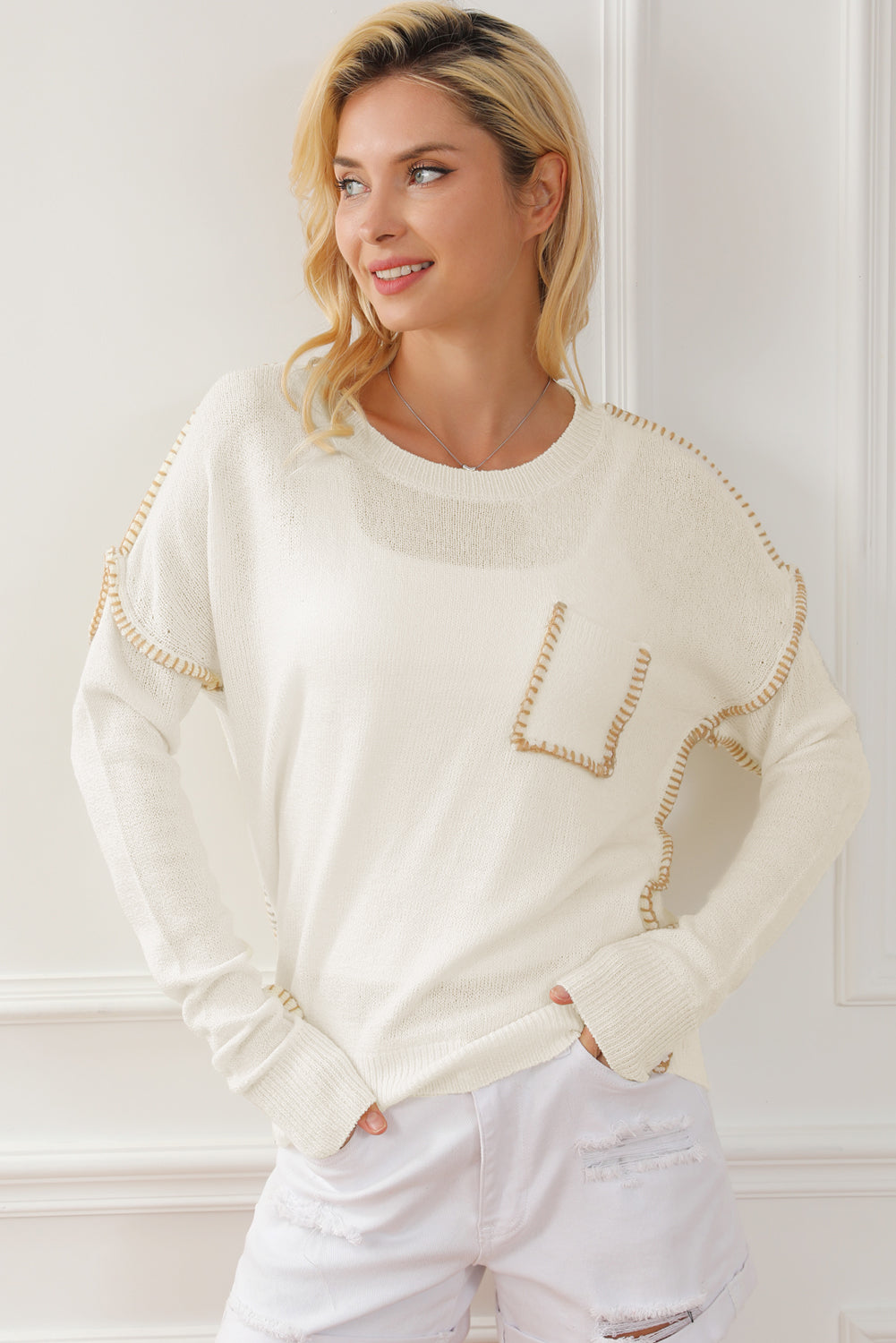 Beige sweater featuring exposed stitching, drop shoulder design, and a chest pocket, styled on a mannequin.