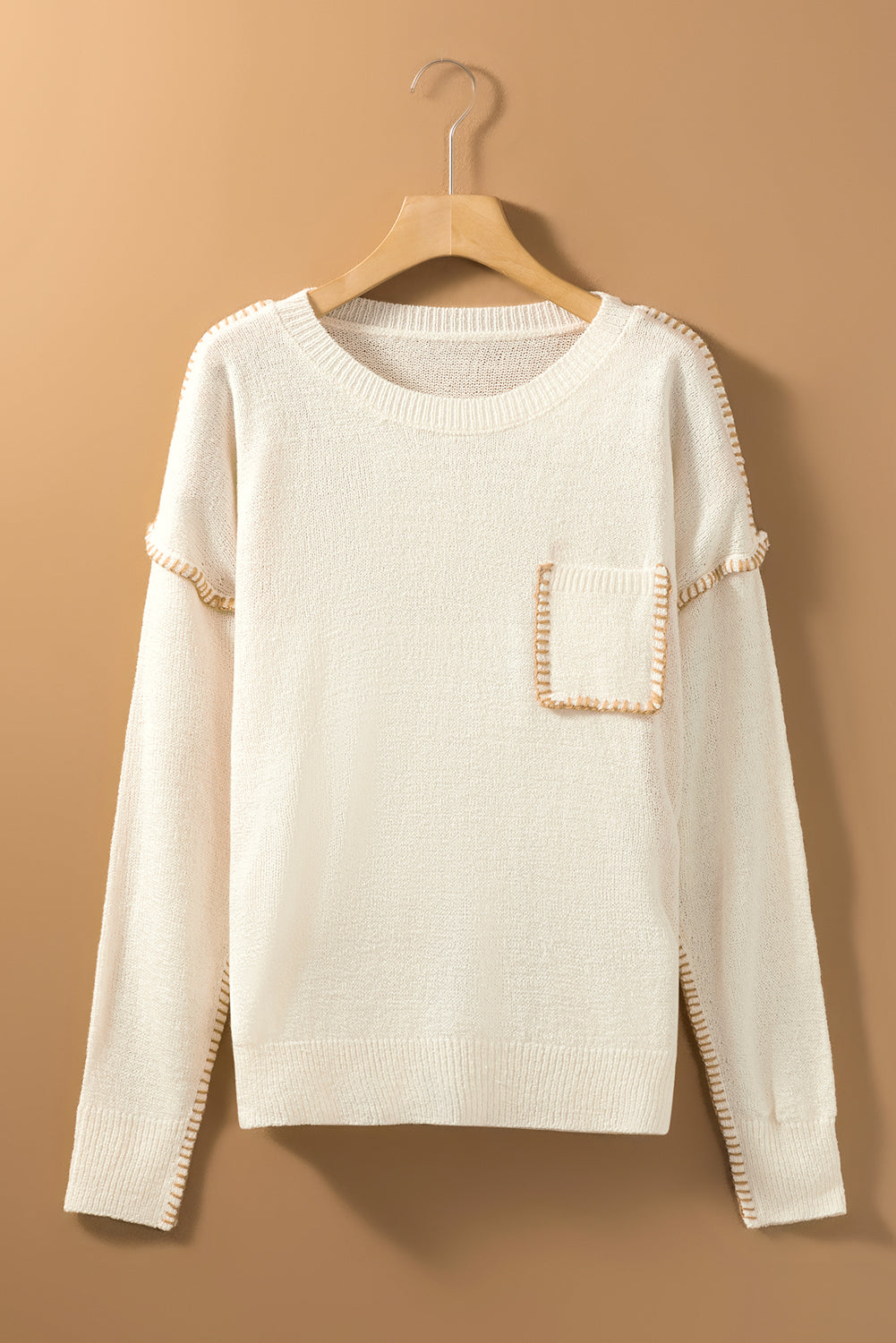 Beige sweater featuring exposed stitching, drop shoulder design, and a chest pocket, styled on a mannequin.