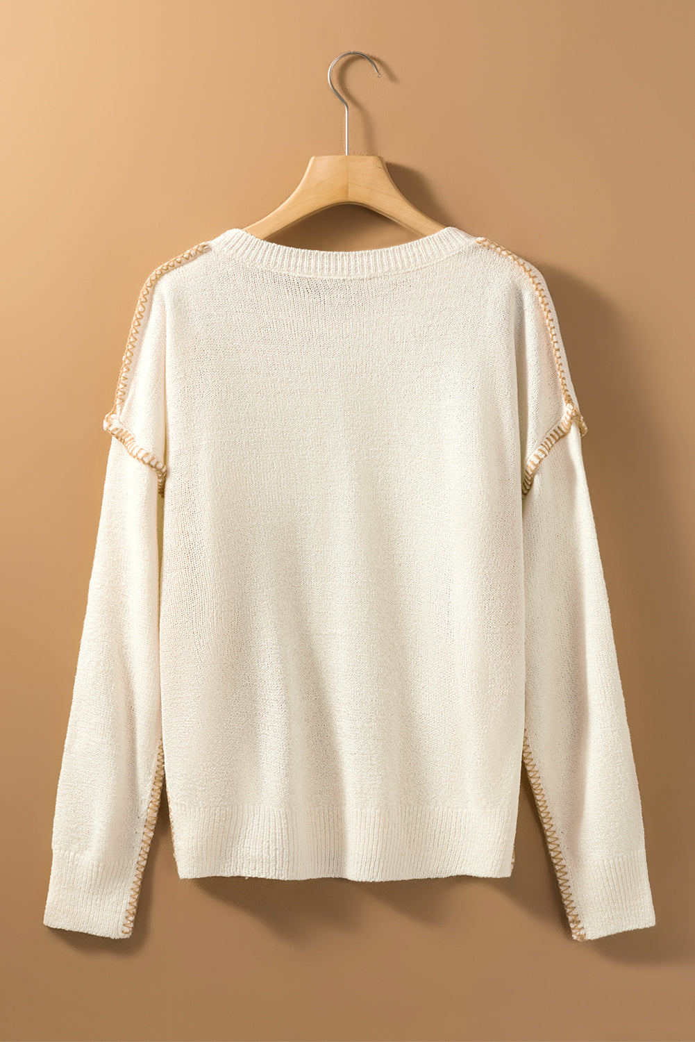 Beige sweater featuring exposed stitching, drop shoulder design, and a chest pocket, styled on a mannequin.