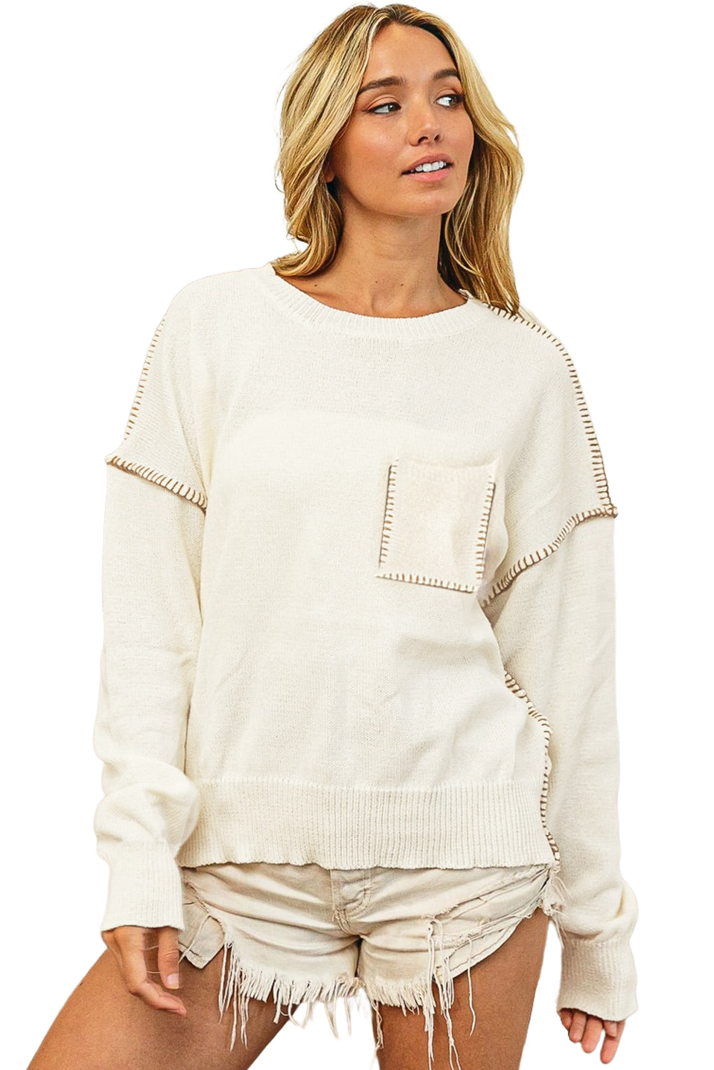 Beige sweater featuring exposed stitching, drop shoulder design, and a chest pocket, styled on a mannequin.