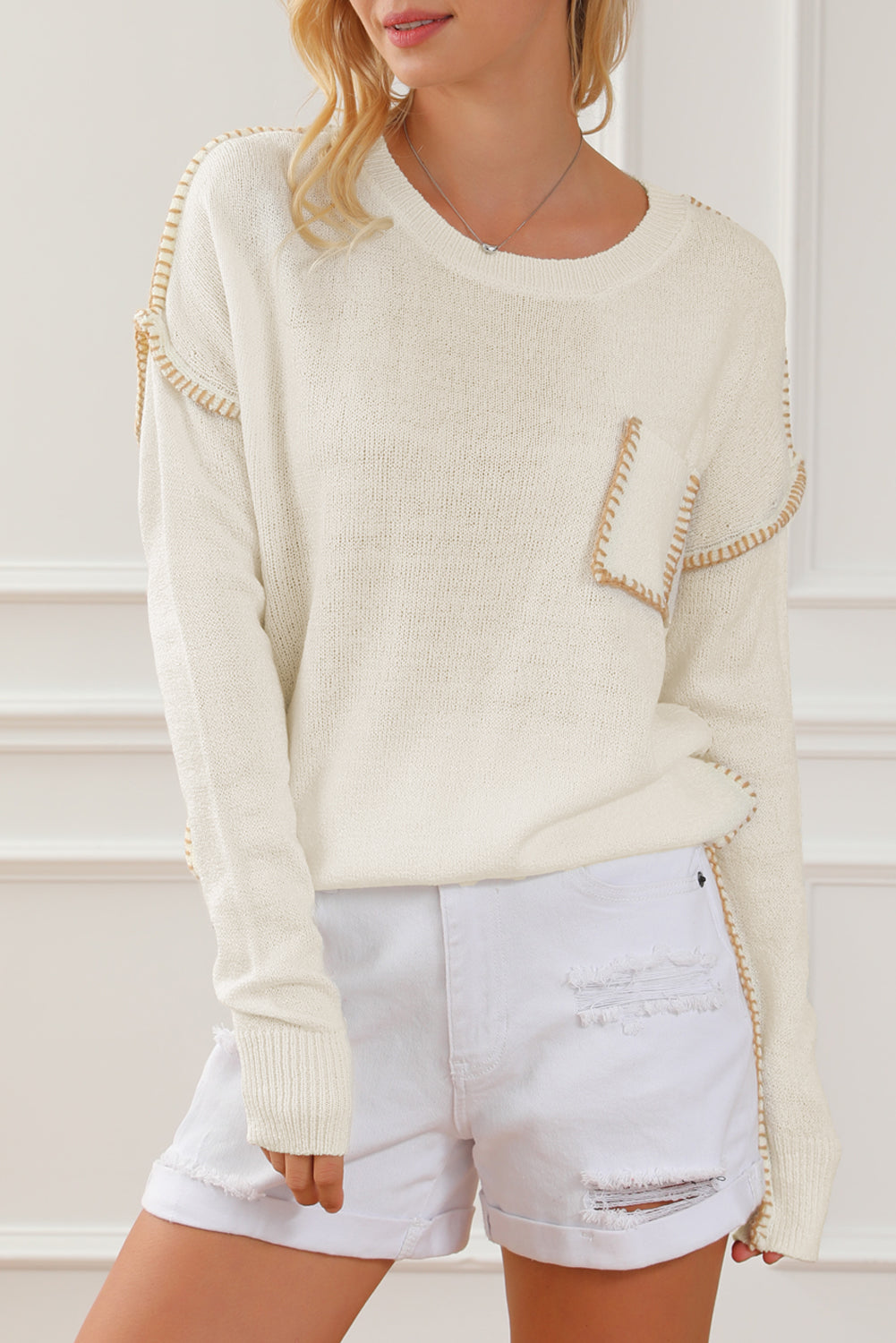 Beige sweater featuring exposed stitching, drop shoulder design, and a chest pocket, styled on a mannequin.