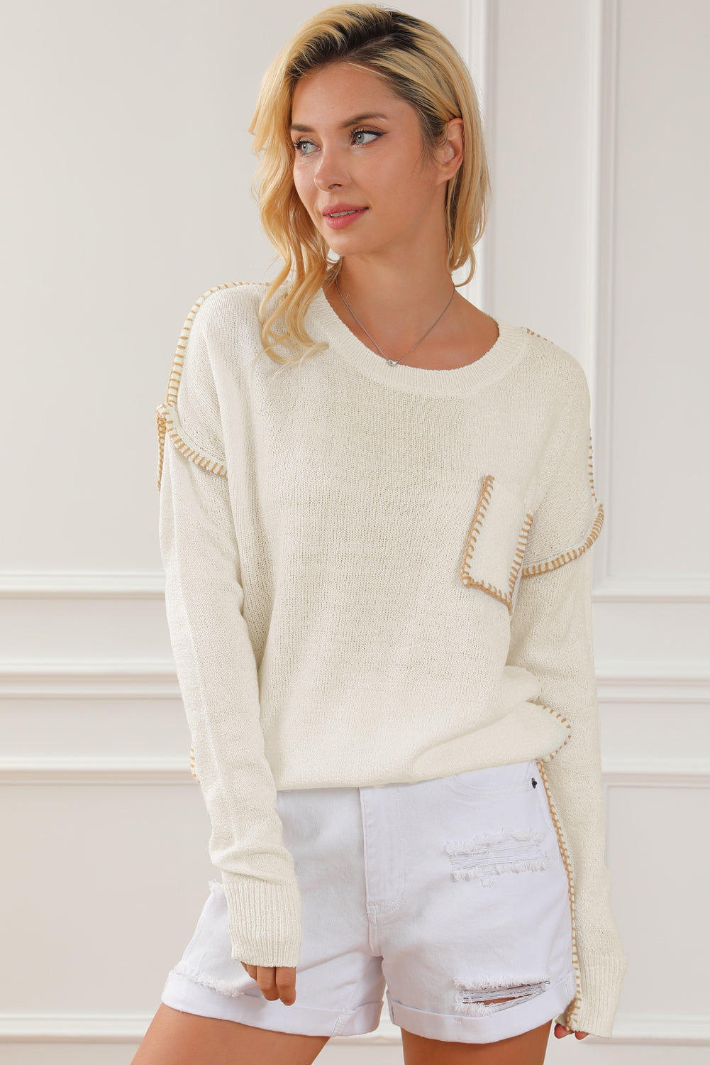 Beige sweater featuring exposed stitching, drop shoulder design, and a chest pocket, styled on a mannequin.