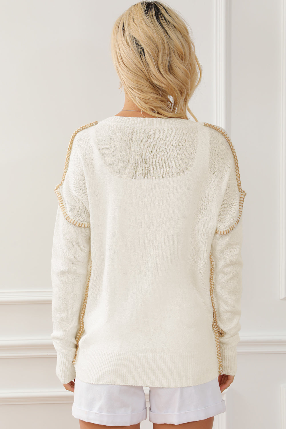 Beige sweater featuring exposed stitching, drop shoulder design, and a chest pocket, styled on a mannequin.