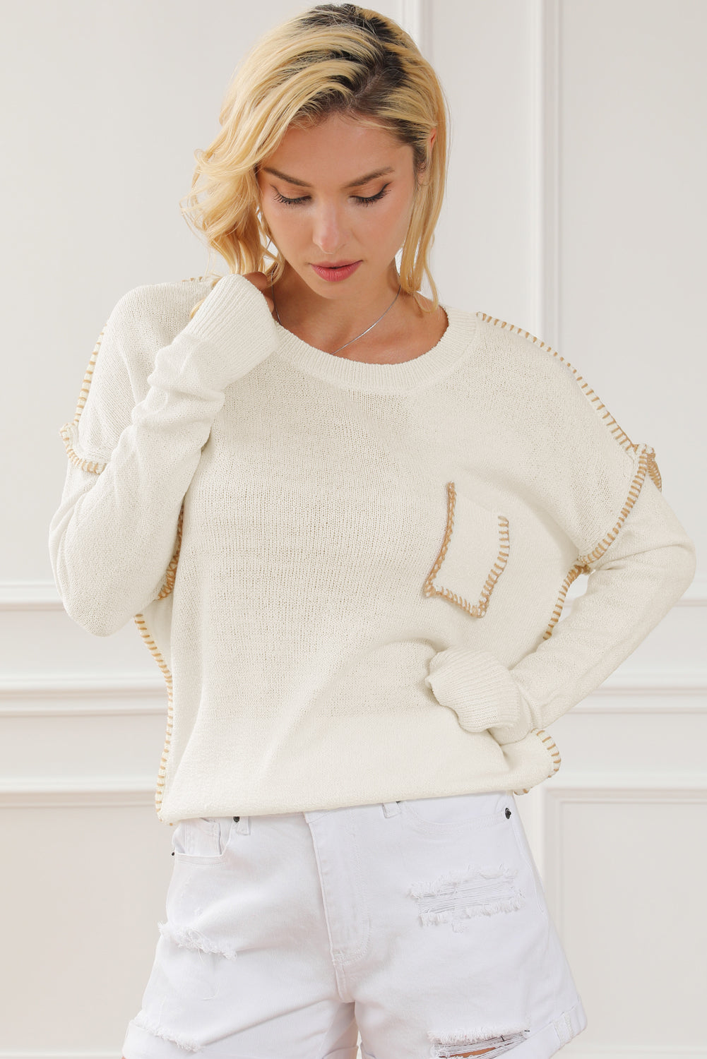 Beige sweater featuring exposed stitching, drop shoulder design, and a chest pocket, styled on a mannequin.