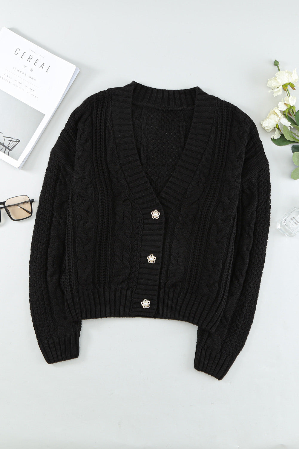 A stylish black knit cardigan featuring button closures, deep v-neck, and long drop-shoulder sleeves, perfect for layering in cold weather.