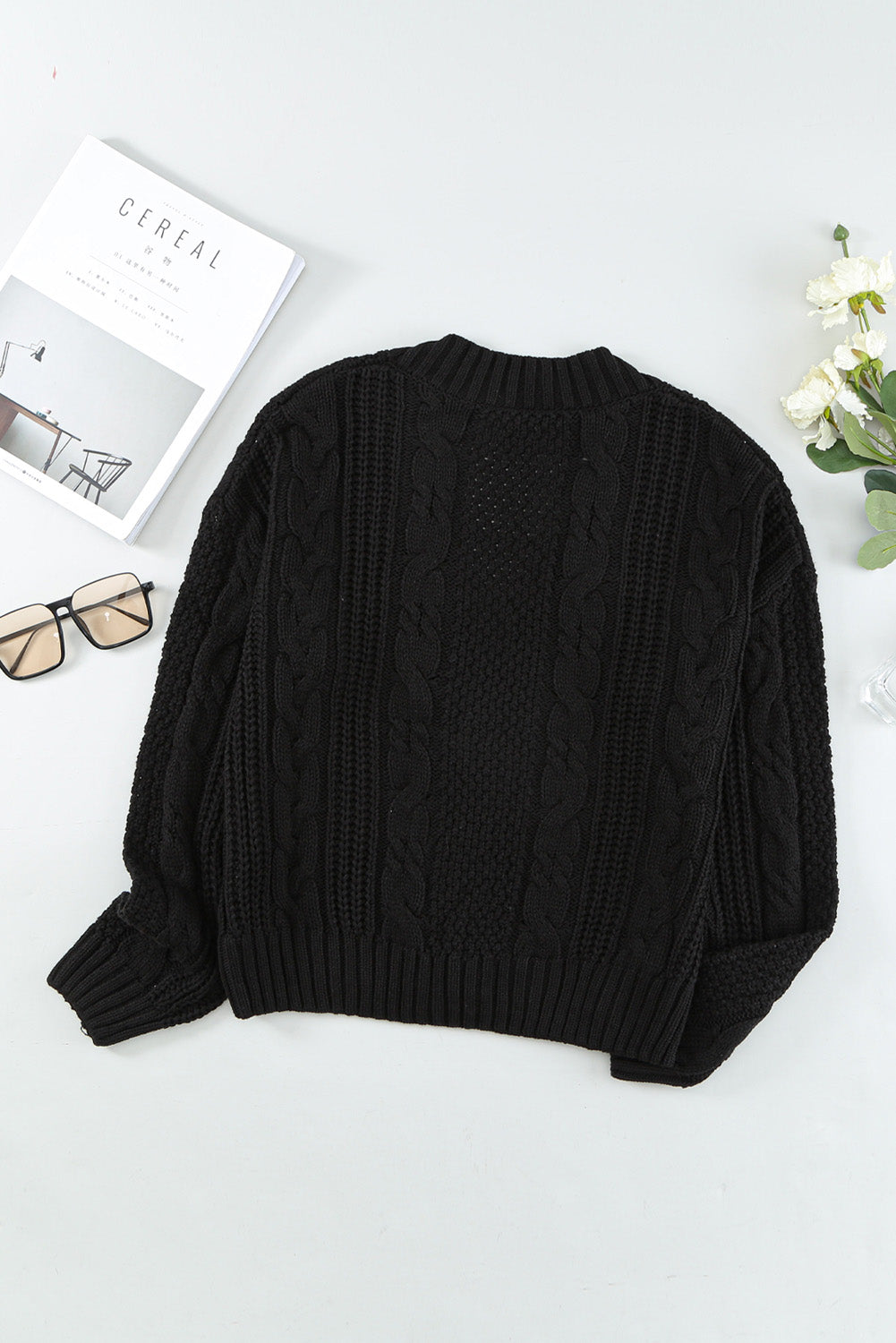 A stylish black knit cardigan featuring button closures, deep v-neck, and long drop-shoulder sleeves, perfect for layering in cold weather.