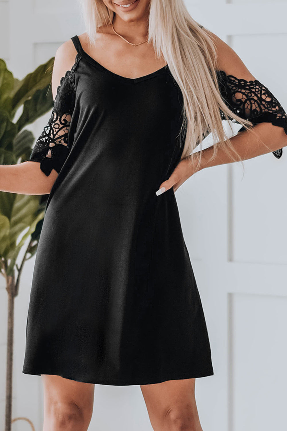 A stylish black mini dress featuring cold shoulder design, V-neckline, and lace sleeves, perfect for a chic and sexy look.