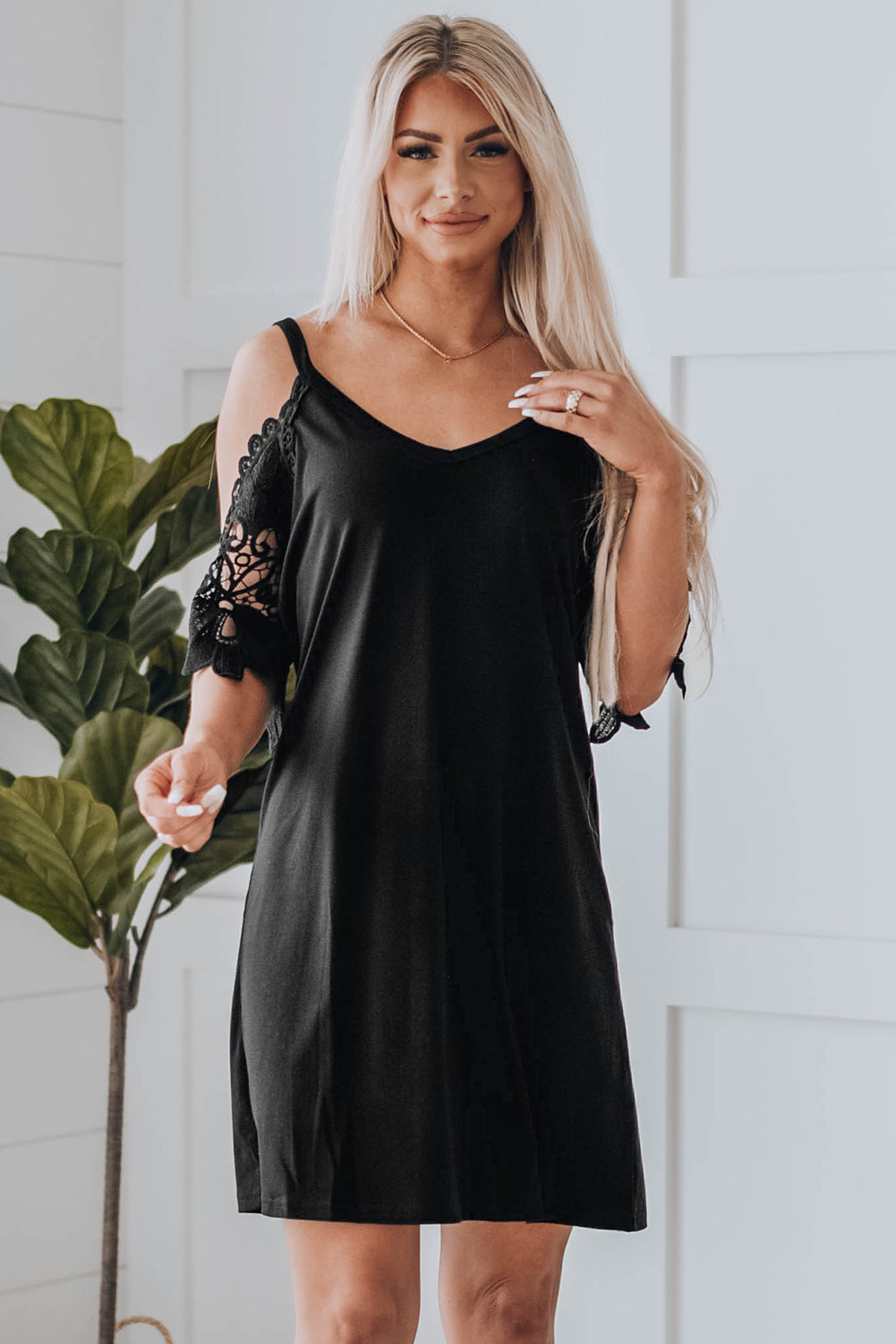 A stylish black mini dress featuring cold shoulder design, V-neckline, and lace sleeves, perfect for a chic and sexy look.