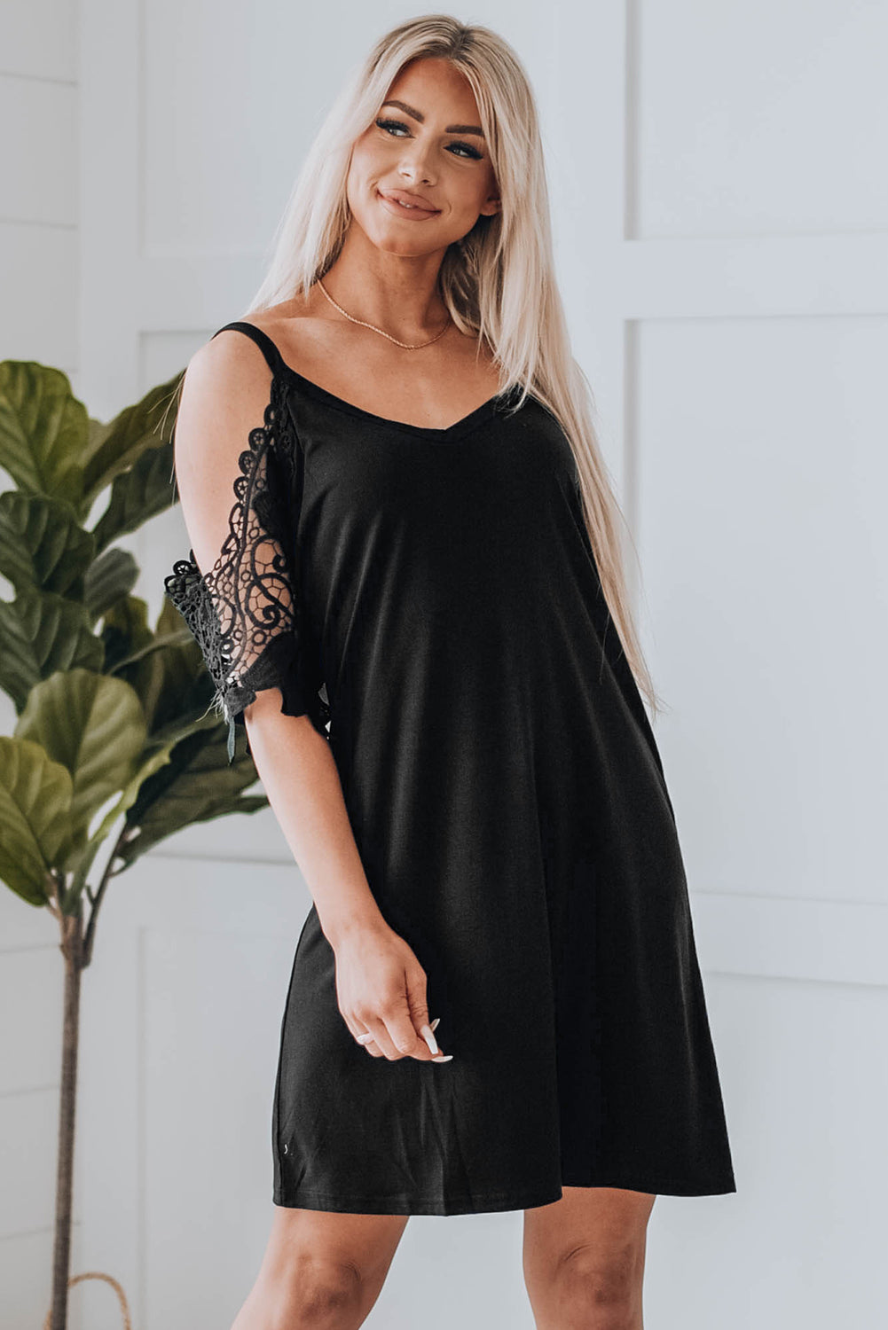 A stylish black mini dress featuring cold shoulder design, V-neckline, and lace sleeves, perfect for a chic and sexy look.