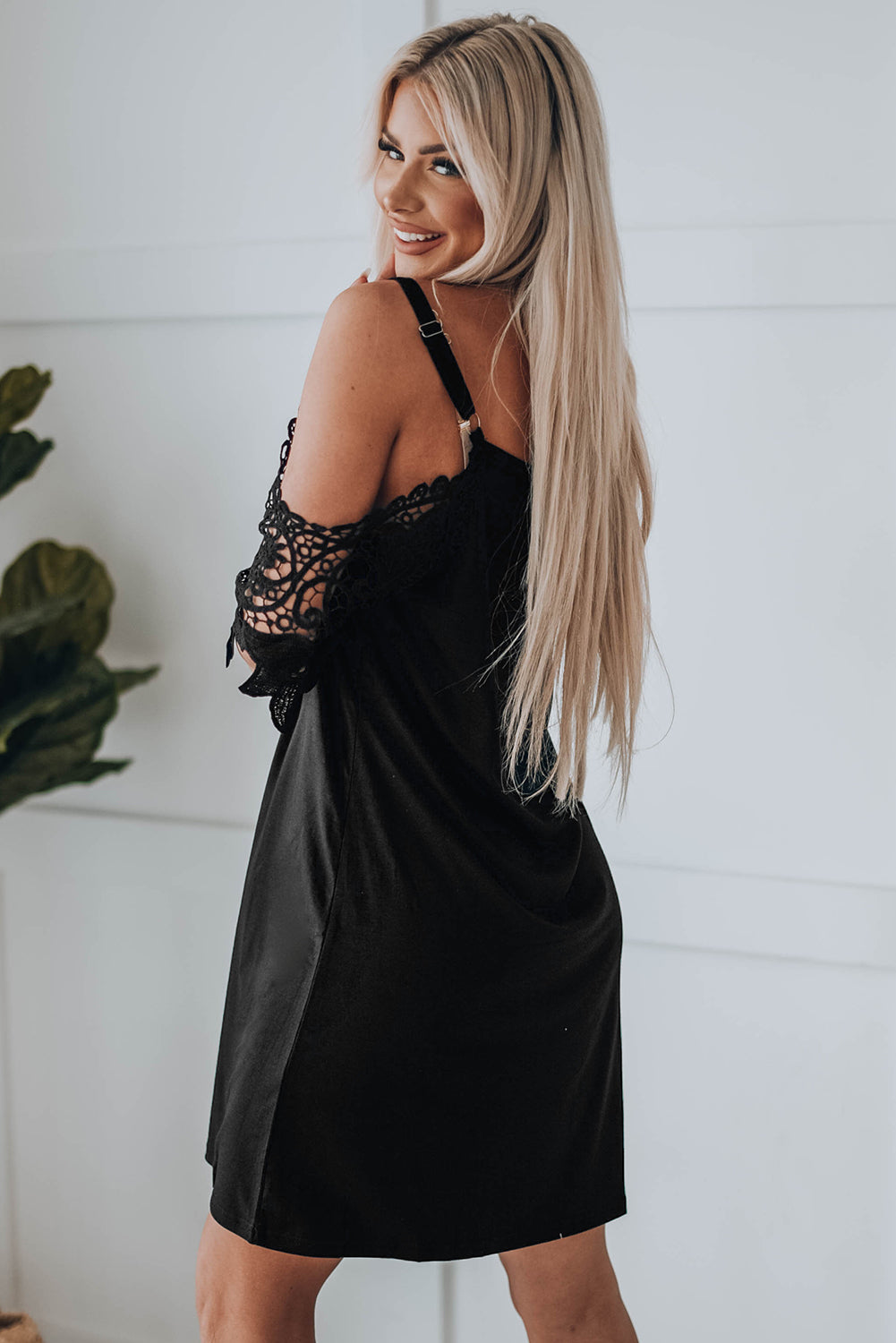 A stylish black mini dress featuring cold shoulder design, V-neckline, and lace sleeves, perfect for a chic and sexy look.