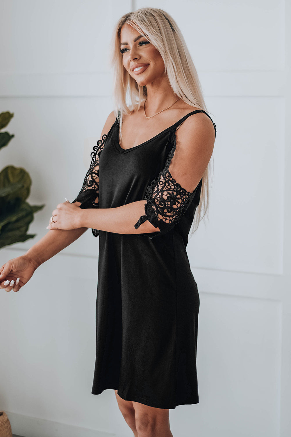 A stylish black mini dress featuring cold shoulder design, V-neckline, and lace sleeves, perfect for a chic and sexy look.