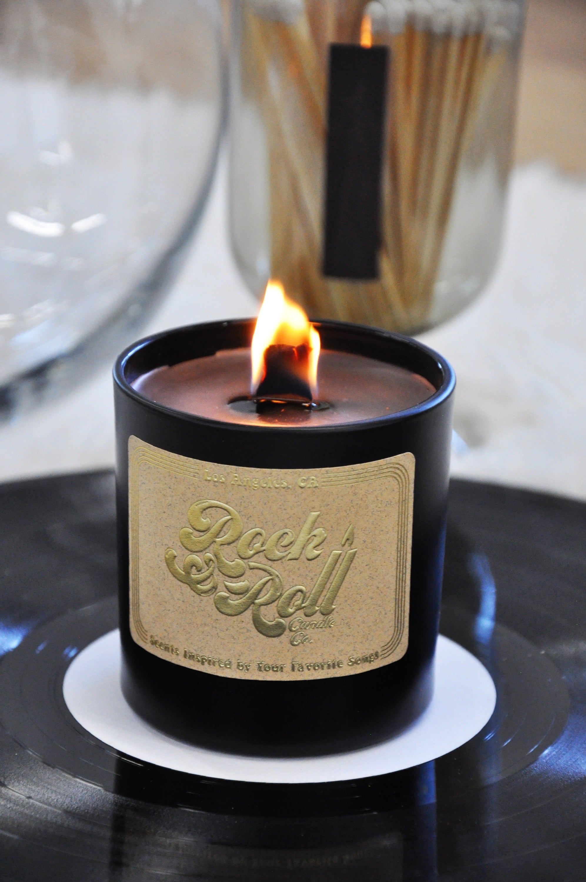 Black Magic Woman candle in a sleek black container, featuring a warm glow and a rich aroma of salted caramel and vanilla.