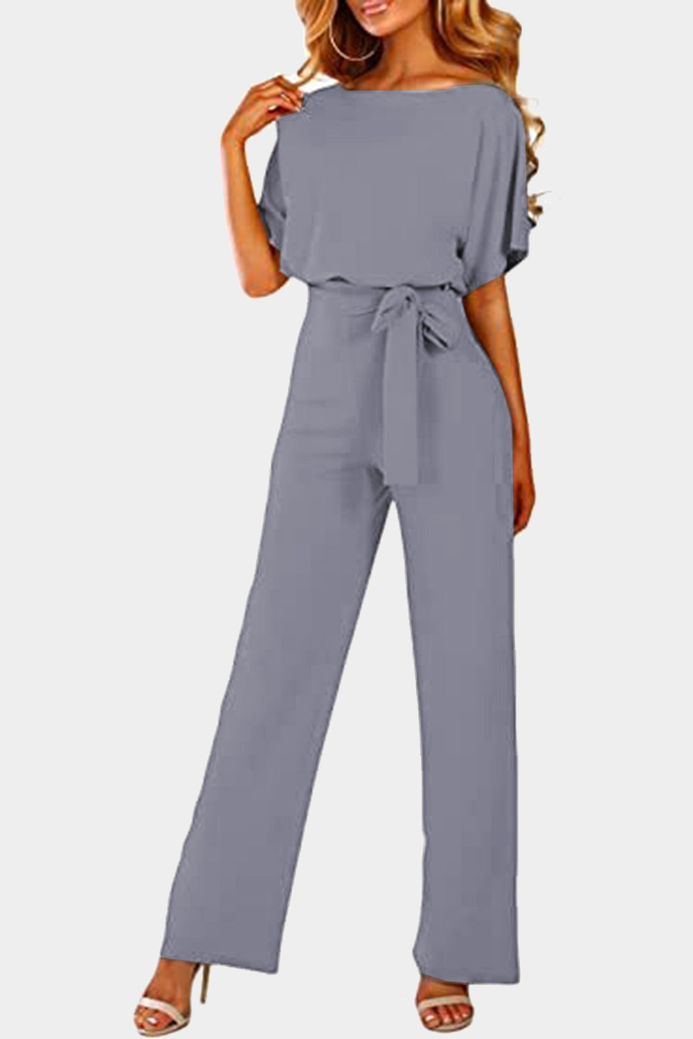 A stylish woman wearing a blue belted wide leg jumpsuit with batwing sleeves, showcasing a chic and glamorous look.