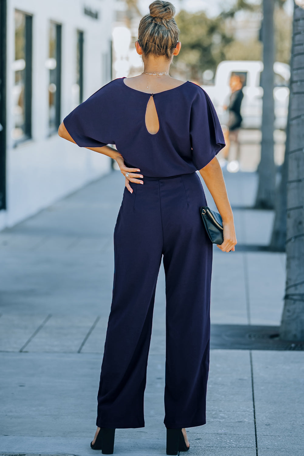 A stylish woman wearing a blue belted wide leg jumpsuit with batwing sleeves, showcasing a chic and glamorous look.