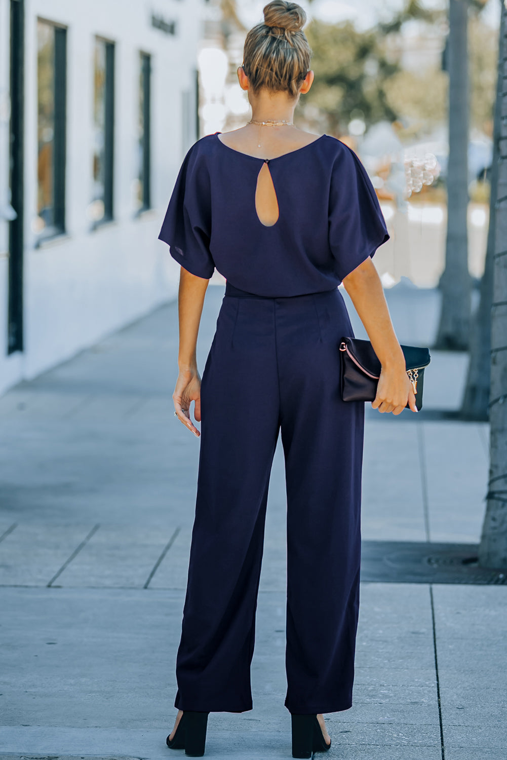 A stylish woman wearing a blue belted wide leg jumpsuit with batwing sleeves, showcasing a chic and glamorous look.