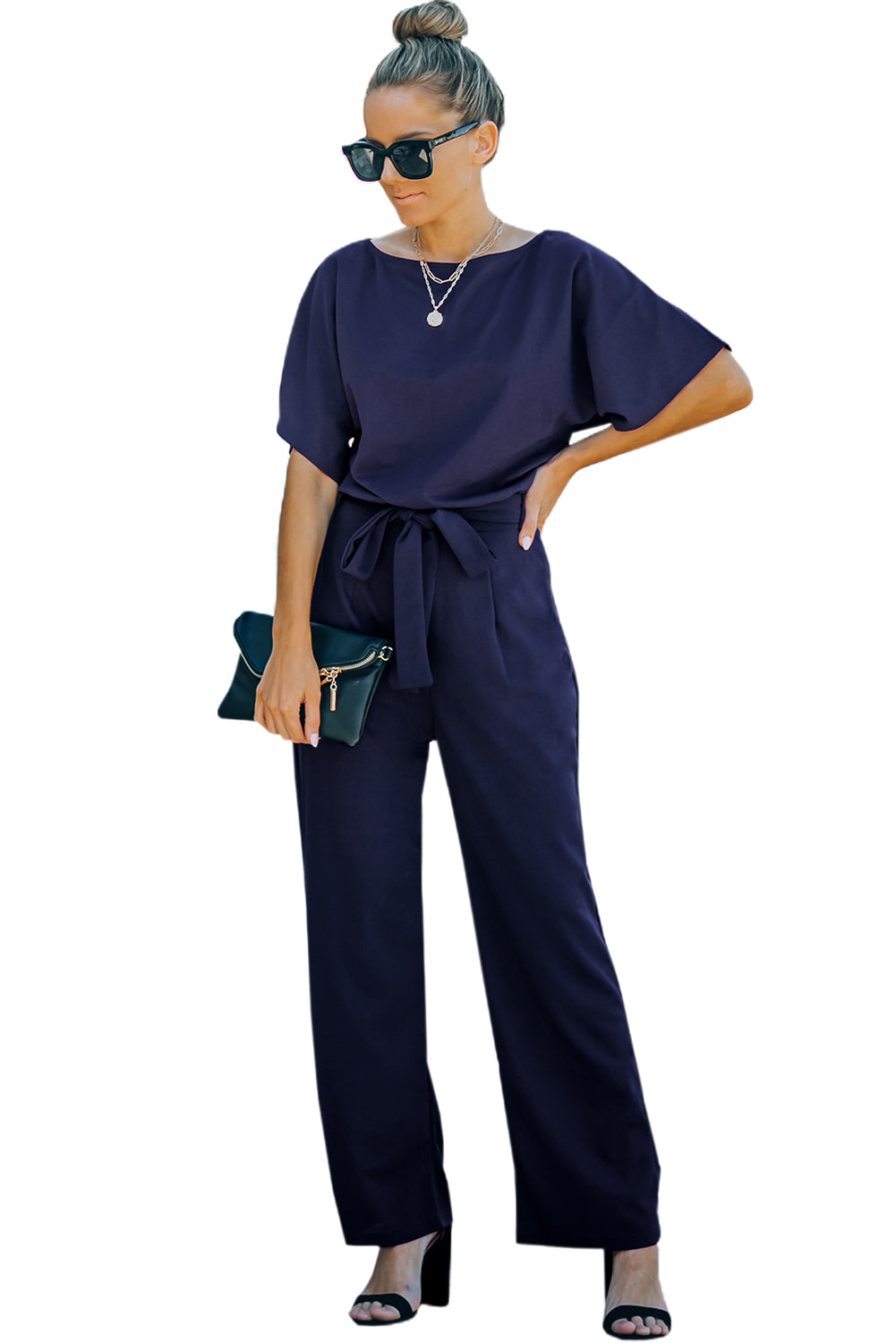 A stylish woman wearing a blue belted wide leg jumpsuit with batwing sleeves, showcasing a chic and glamorous look.