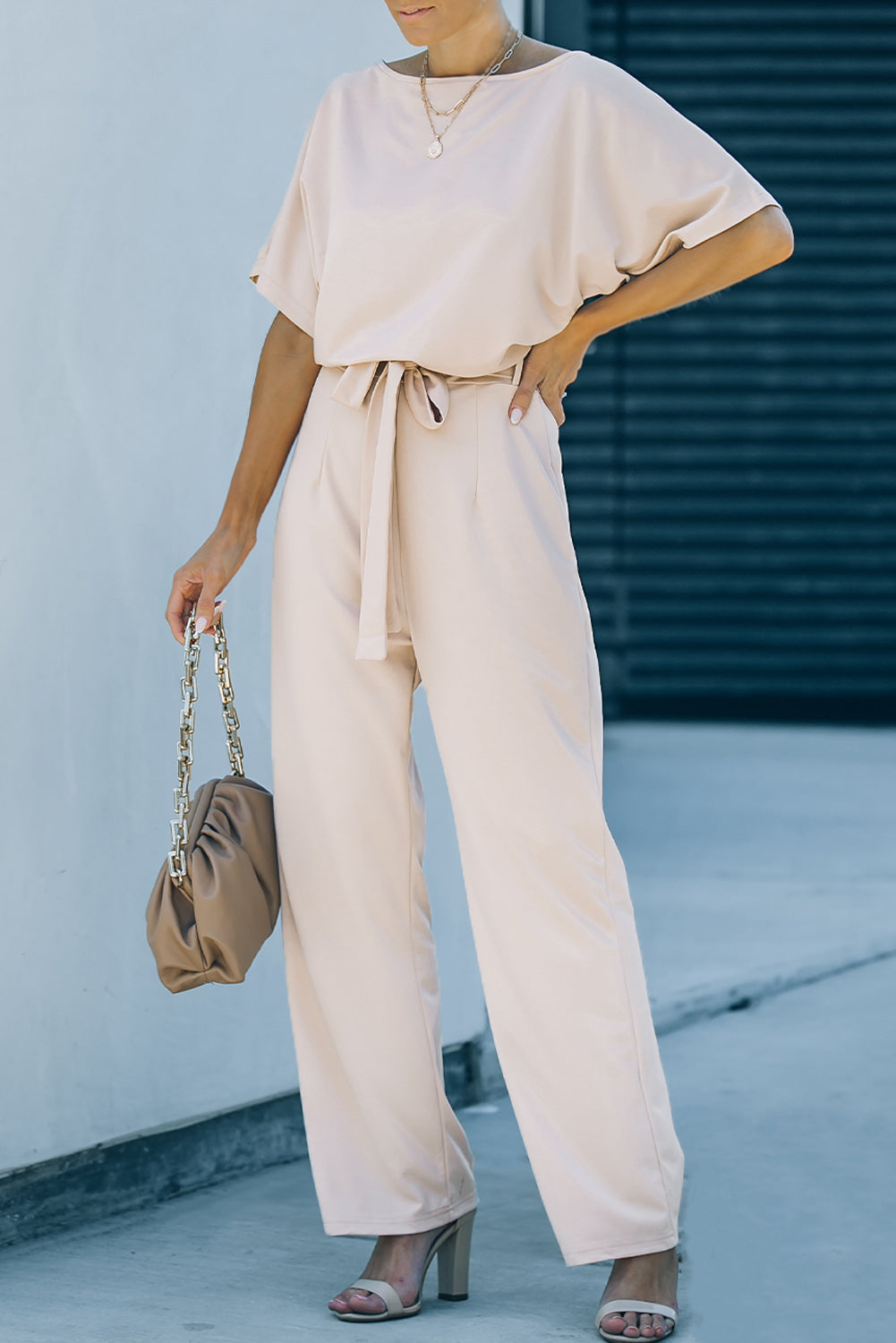 A stylish woman wearing a blue belted wide leg jumpsuit with batwing sleeves, showcasing a chic and glamorous look.