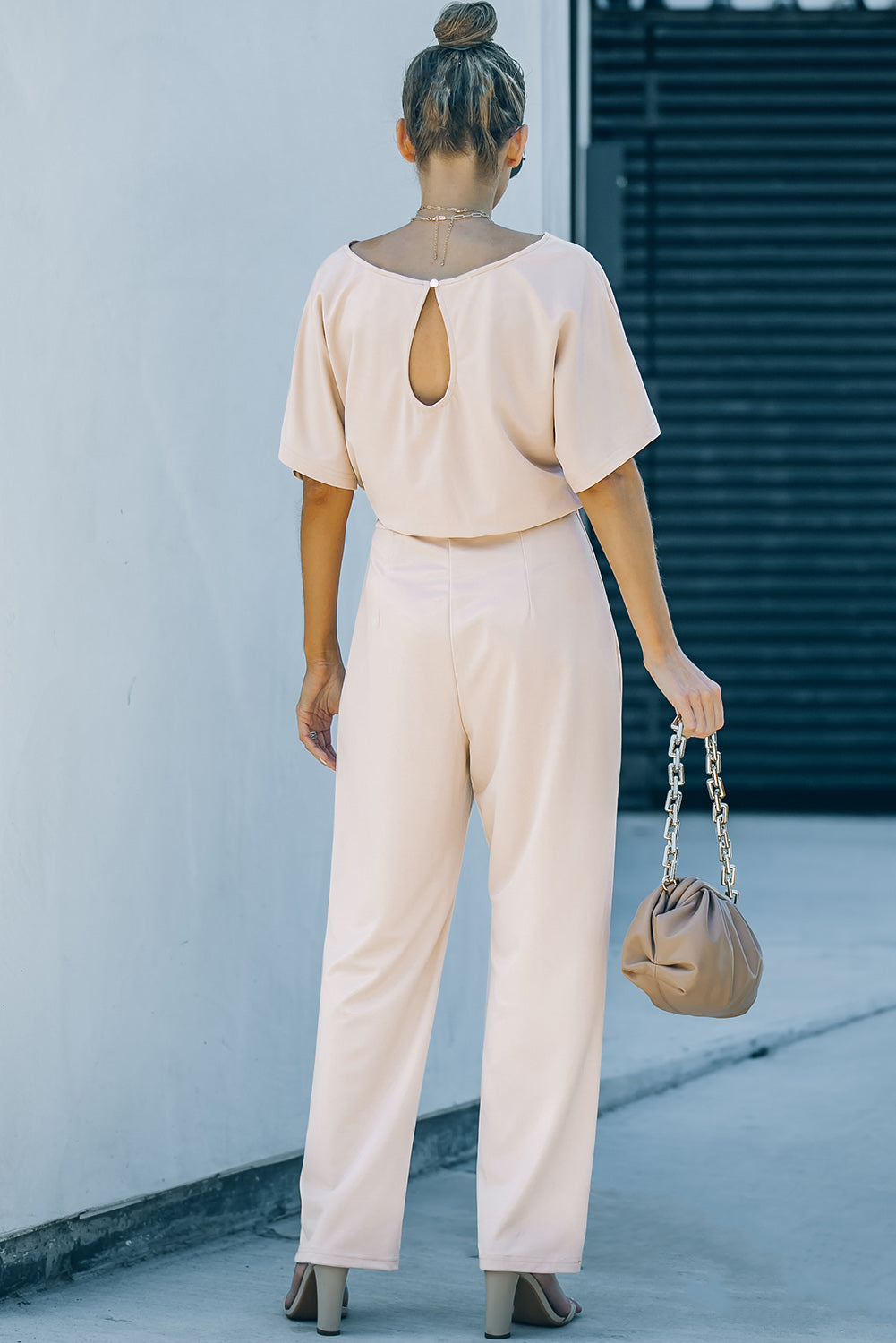 A stylish woman wearing a blue belted wide leg jumpsuit with batwing sleeves, showcasing a chic and glamorous look.