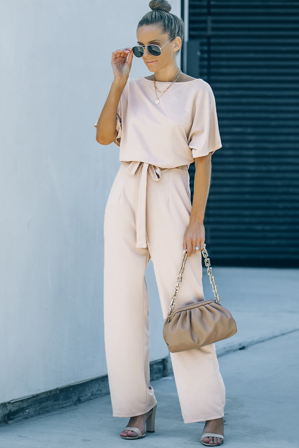 A stylish woman wearing a blue belted wide leg jumpsuit with batwing sleeves, showcasing a chic and glamorous look.