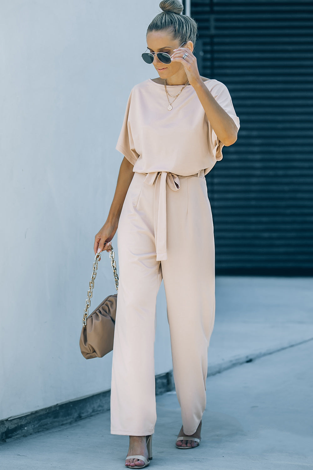 A stylish woman wearing a blue belted wide leg jumpsuit with batwing sleeves, showcasing a chic and glamorous look.